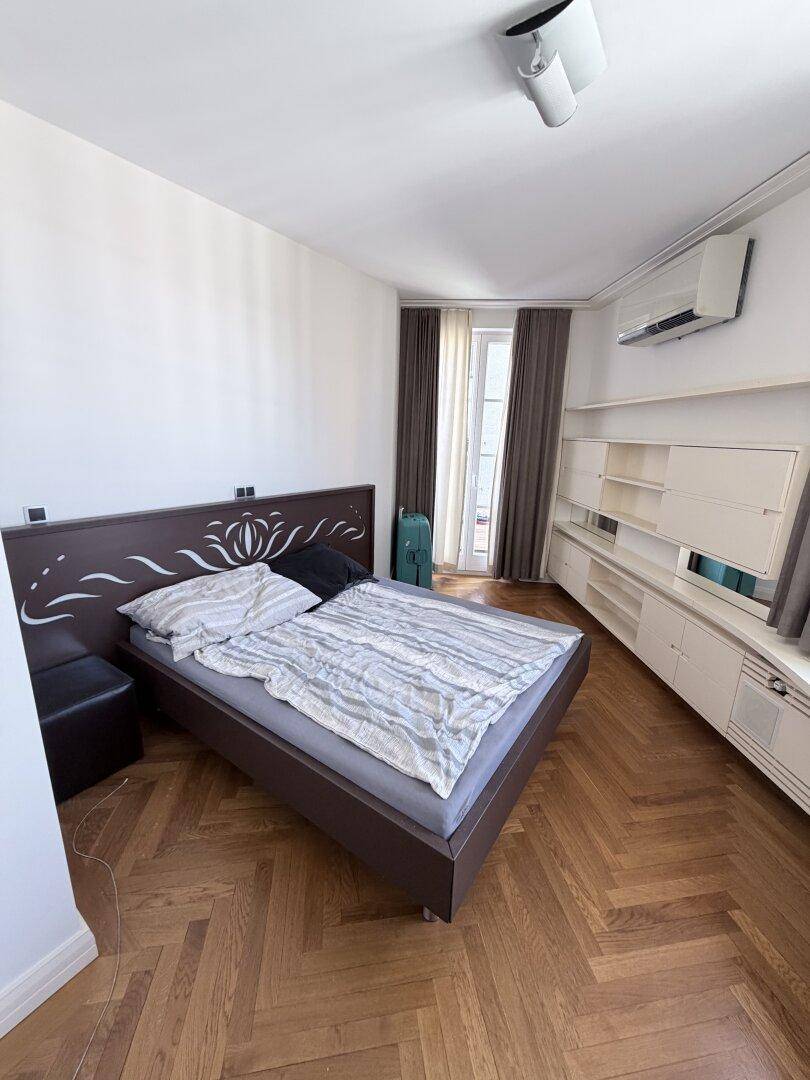 Schlafzimmer mit Parkettboden, Klimaanlage und Zugang zu einem französischen Balkon.