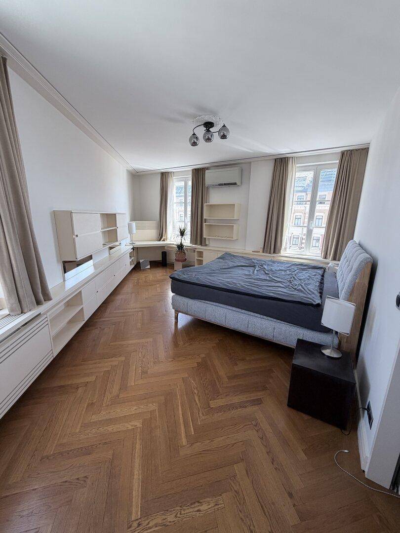 Helles Schlafzimmer mit Parkettboden, großem Bett und Einbauschränken.