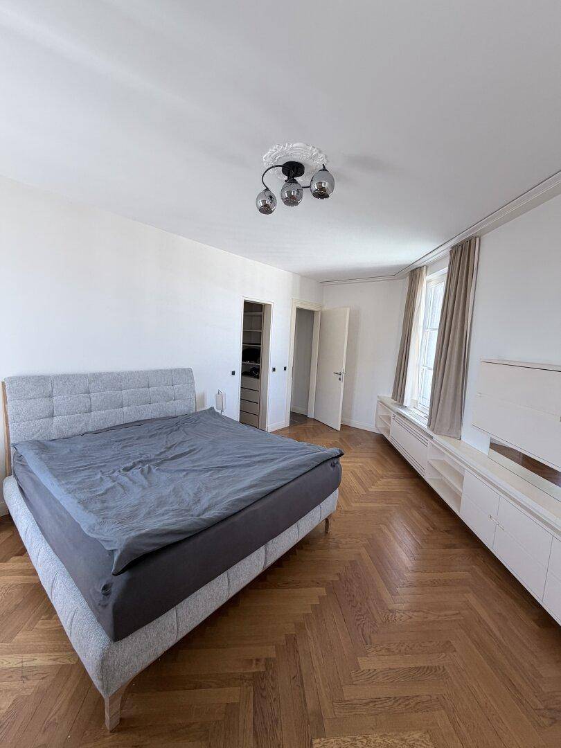 Geräumiges Schlafzimmer mit Parkettboden, großem Bett und Zugang zum begehbaren Kleiderschrank.