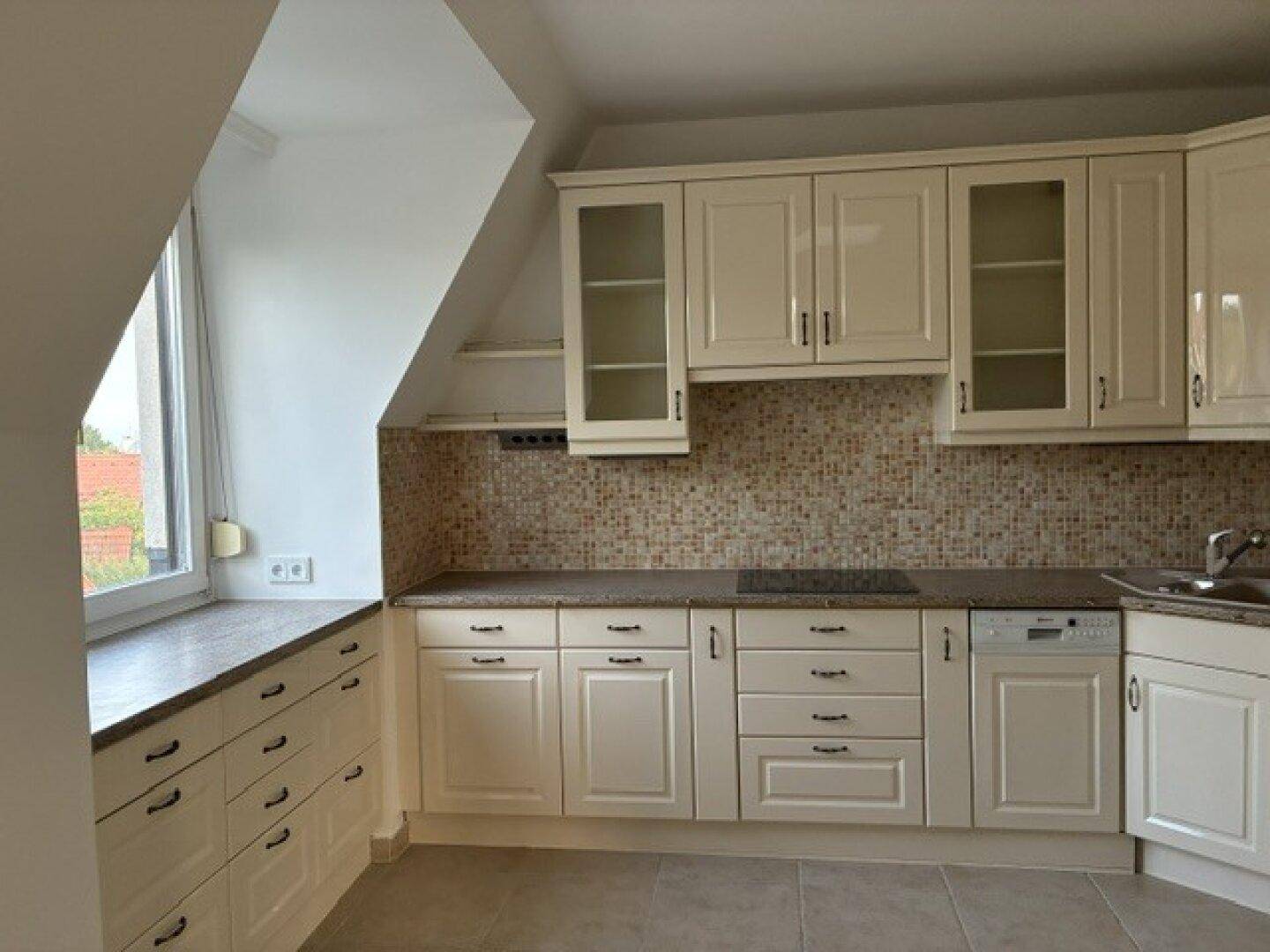 Helle Einbauküche mit cremefarbenen Schränken, Mosaikfliesen und praktischer Dachschräge.