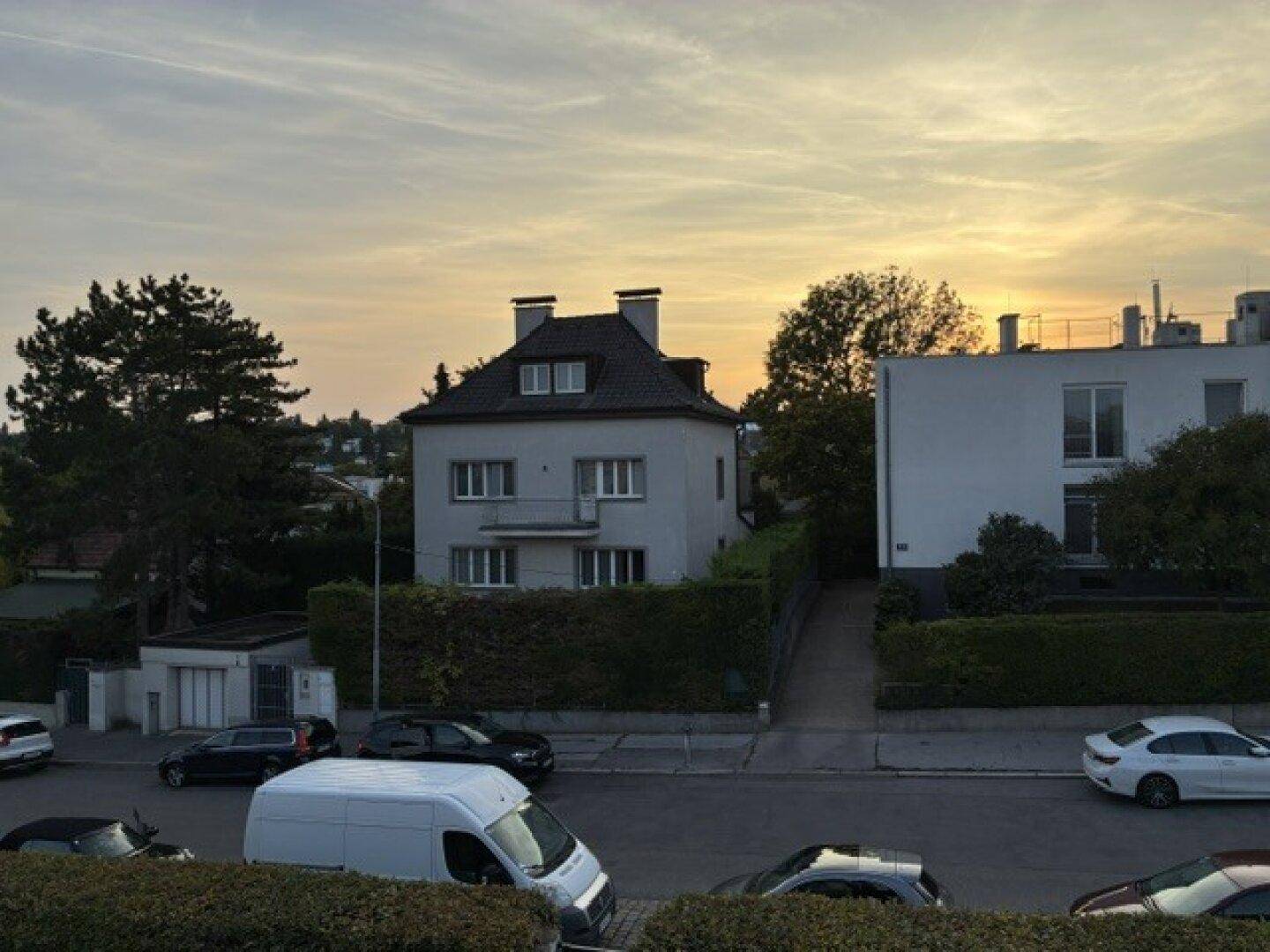 Wohnhausfassade bei Sonnenuntergang, umgeben von einer gepflegten Hecke und Bäumen.