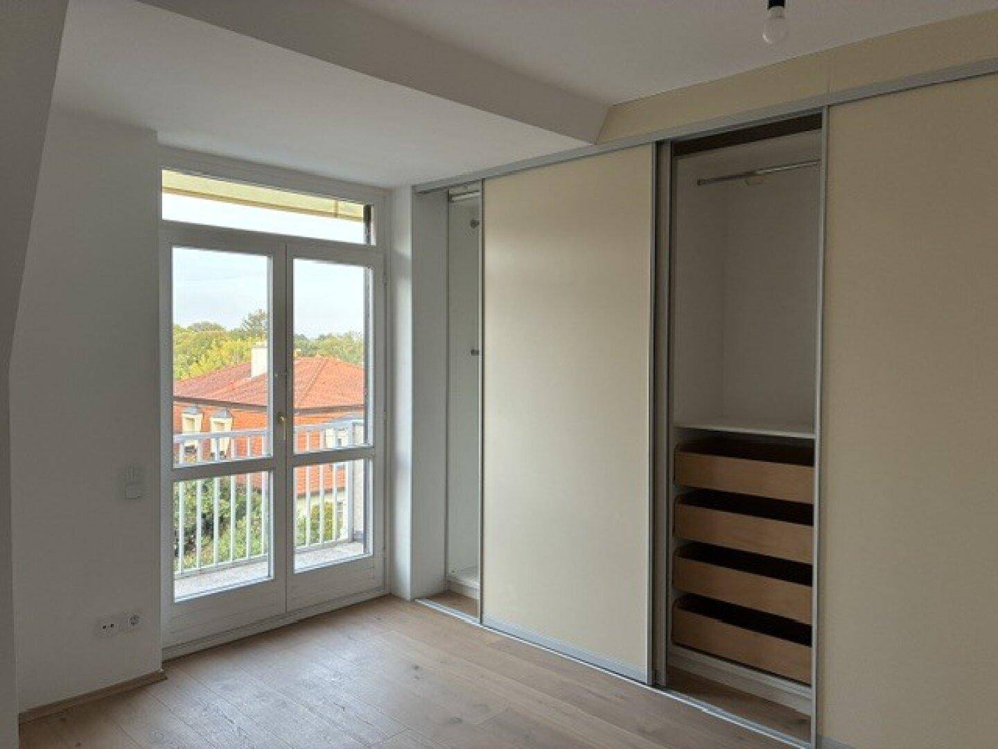 Schlafzimmer mit integriertem Schiebetürenschrank, Holzboden und Zugang zu einem französischen Balkon.