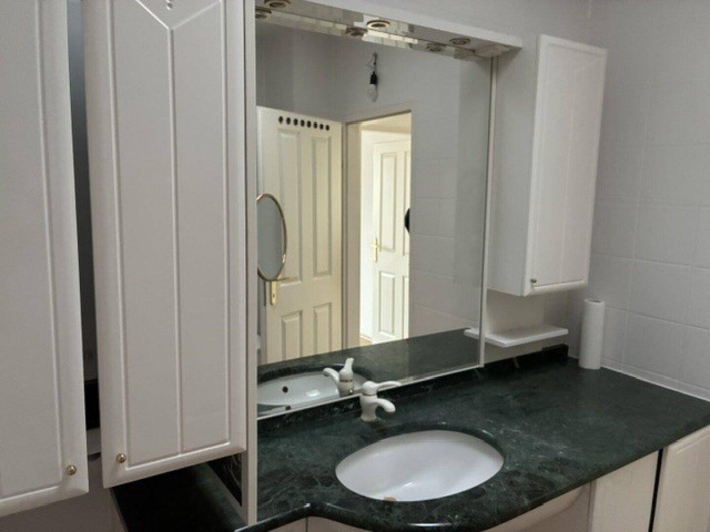 Badezimmer mit Einzelwaschbecken, grünem Marmorwaschtisch und praktischem Spiegelschrank.
