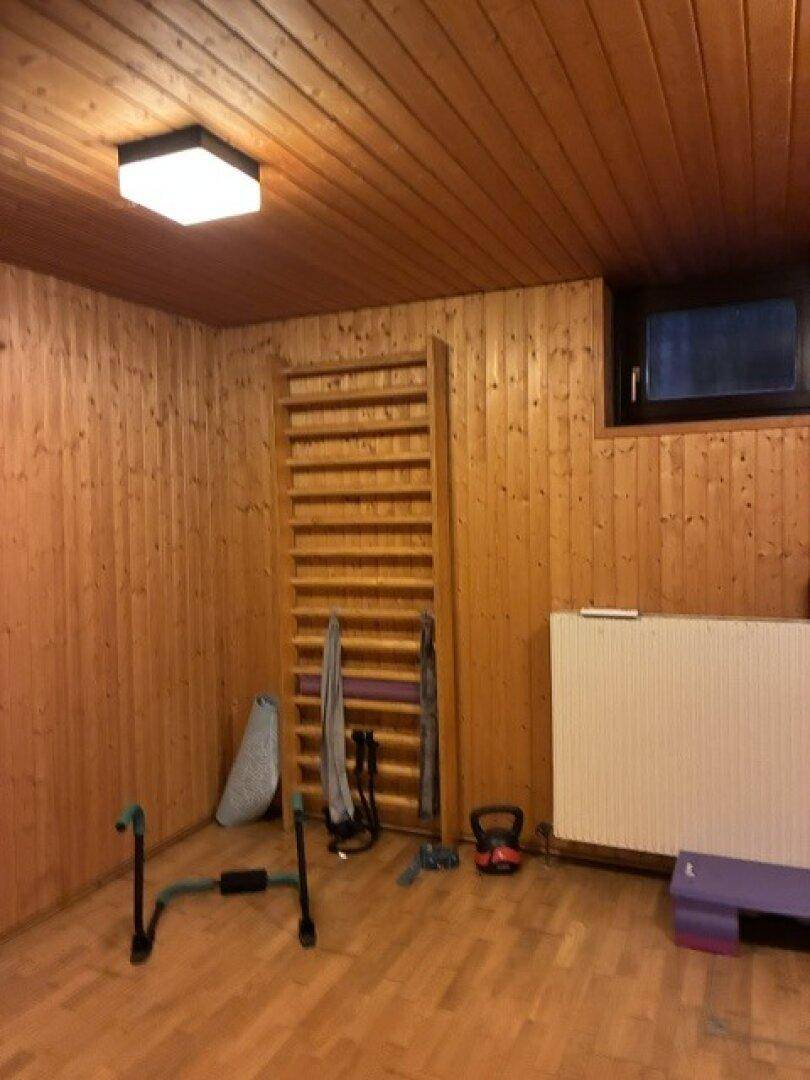 Privater Fitnessraum mit Holzverkleidung, Sprossenwand und verschiedenen Trainingsgeräten.