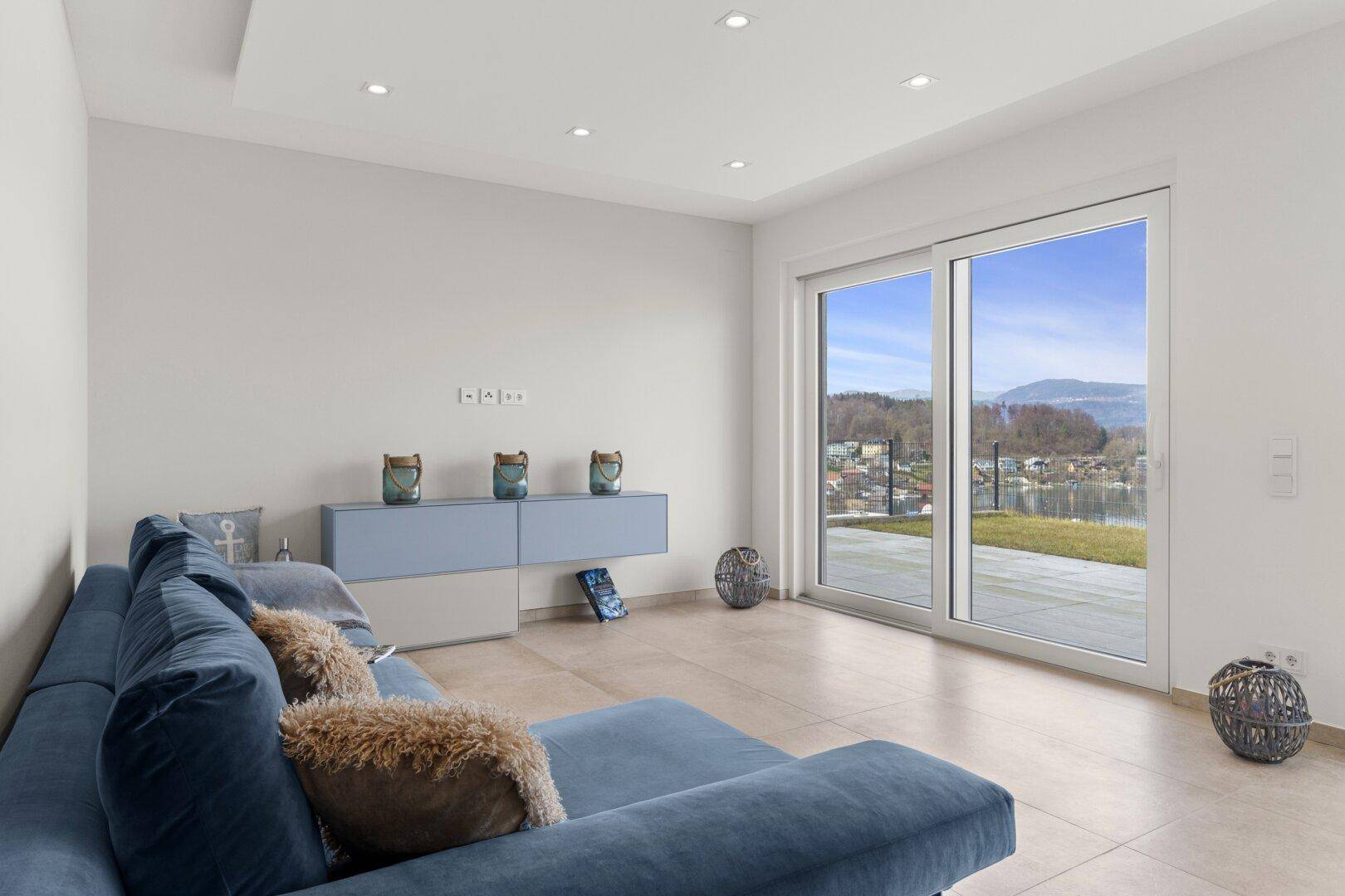 Helles Wohnzimmer mit bequemer Couch und Schiebetüren zur Terrasse mit Seeblick.