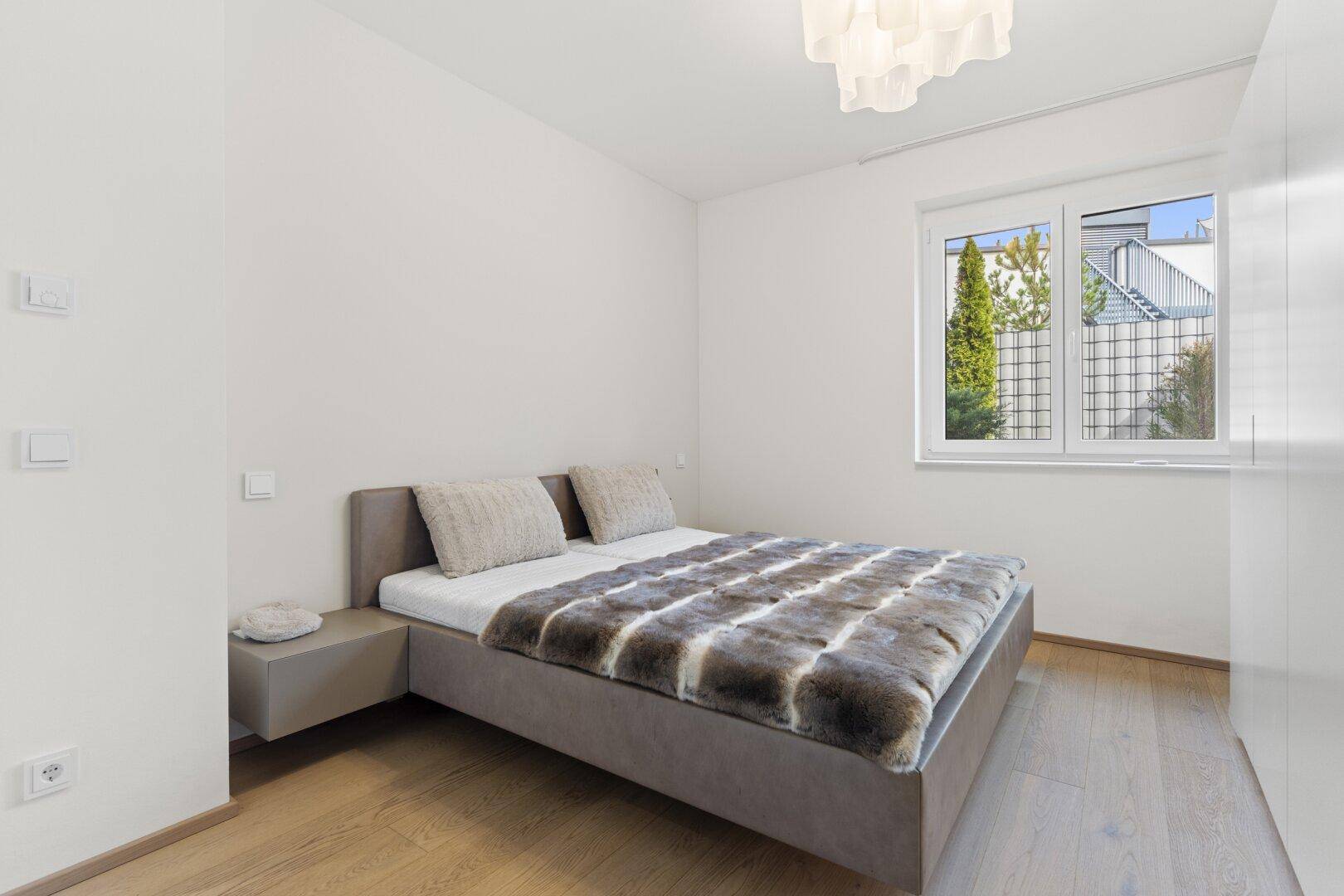 Gemütliches Schlafzimmer mit Holzboden, Doppelbett und Fenster mit Blick ins Grüne.