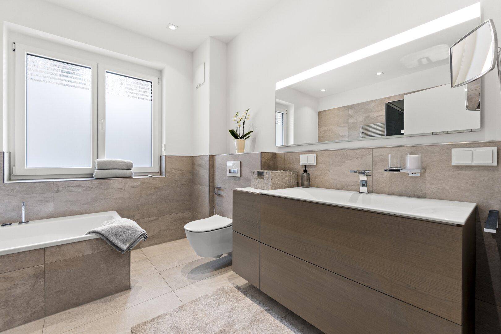 Modernes Badezimmer mit Badewanne, Waschtisch, großem Spiegel und Fenster.