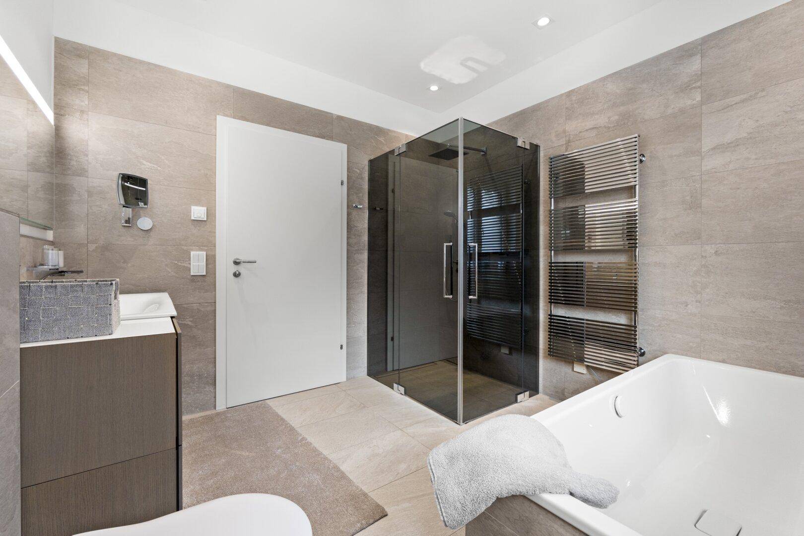 Elegantes Badezimmer mit Glasdusche, Badewanne und beheiztem Handtuchhalter.