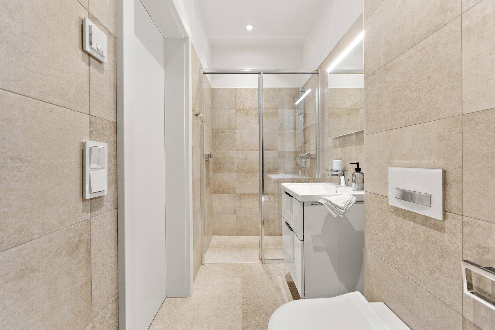 Kompaktes Badezimmer mit Dusche, WC und modernem Waschtisch in hellen Fliesen.
