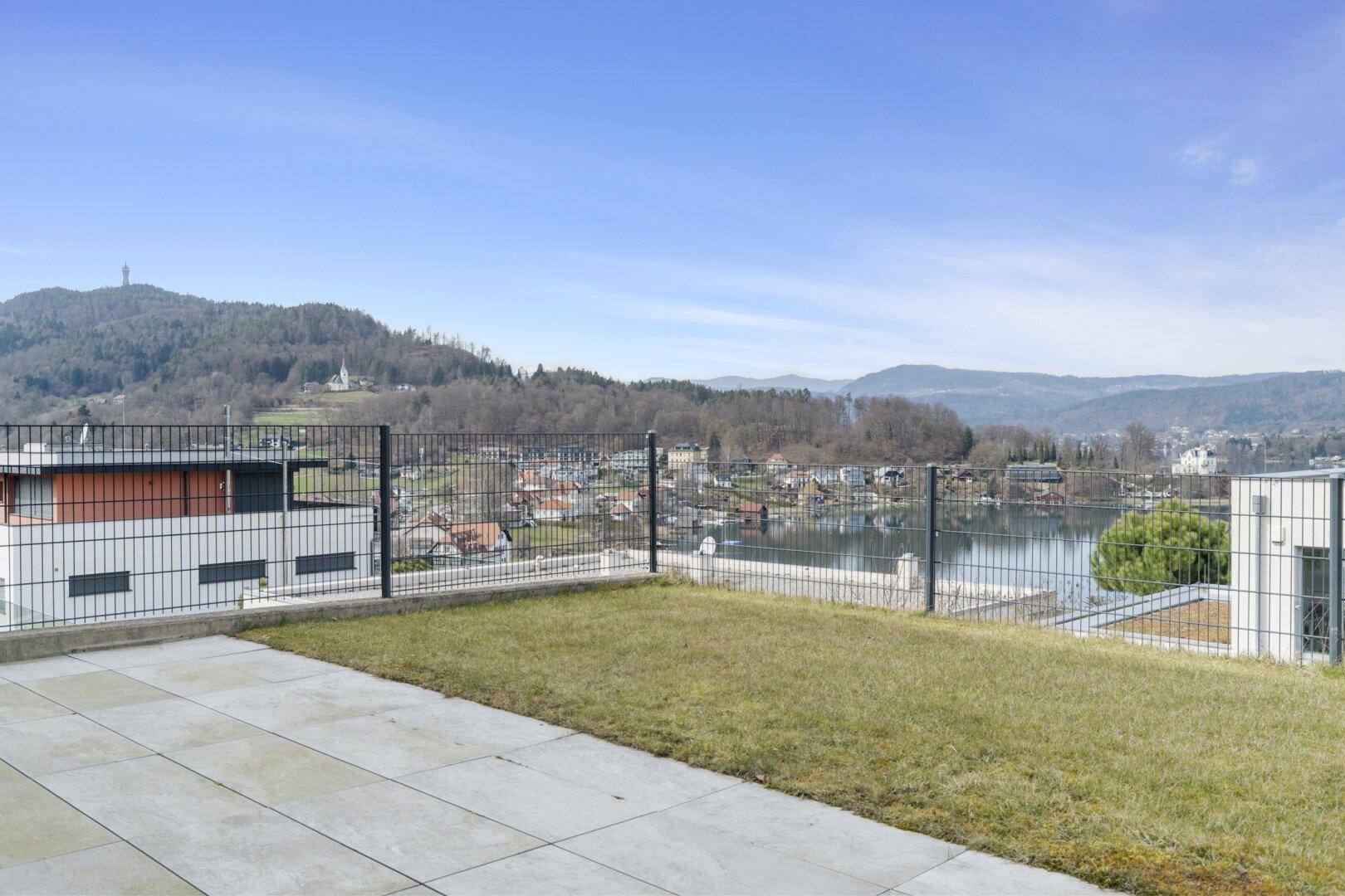 Gepflegte Rasenfläche mit Zaun und weitem Blick auf den See und die Berge.