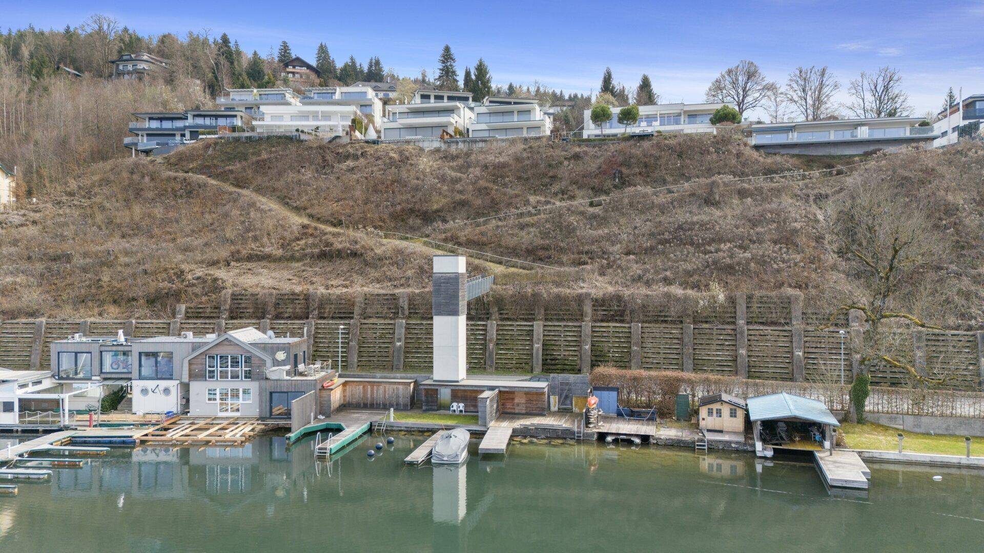 Blick auf die Uferbebauung mit Bootsanlegestellen und einem markanten Turm am See.