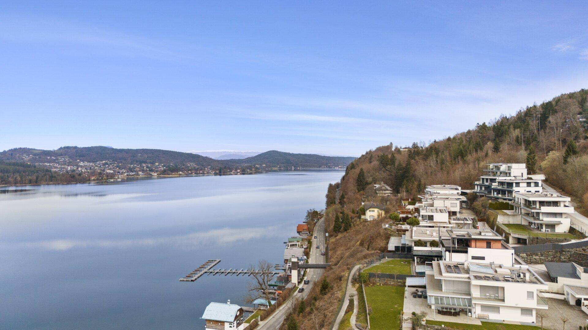Weitläufiger Luftbildblick auf den See, die bewaldeten Hügel und die Uferbebauung.