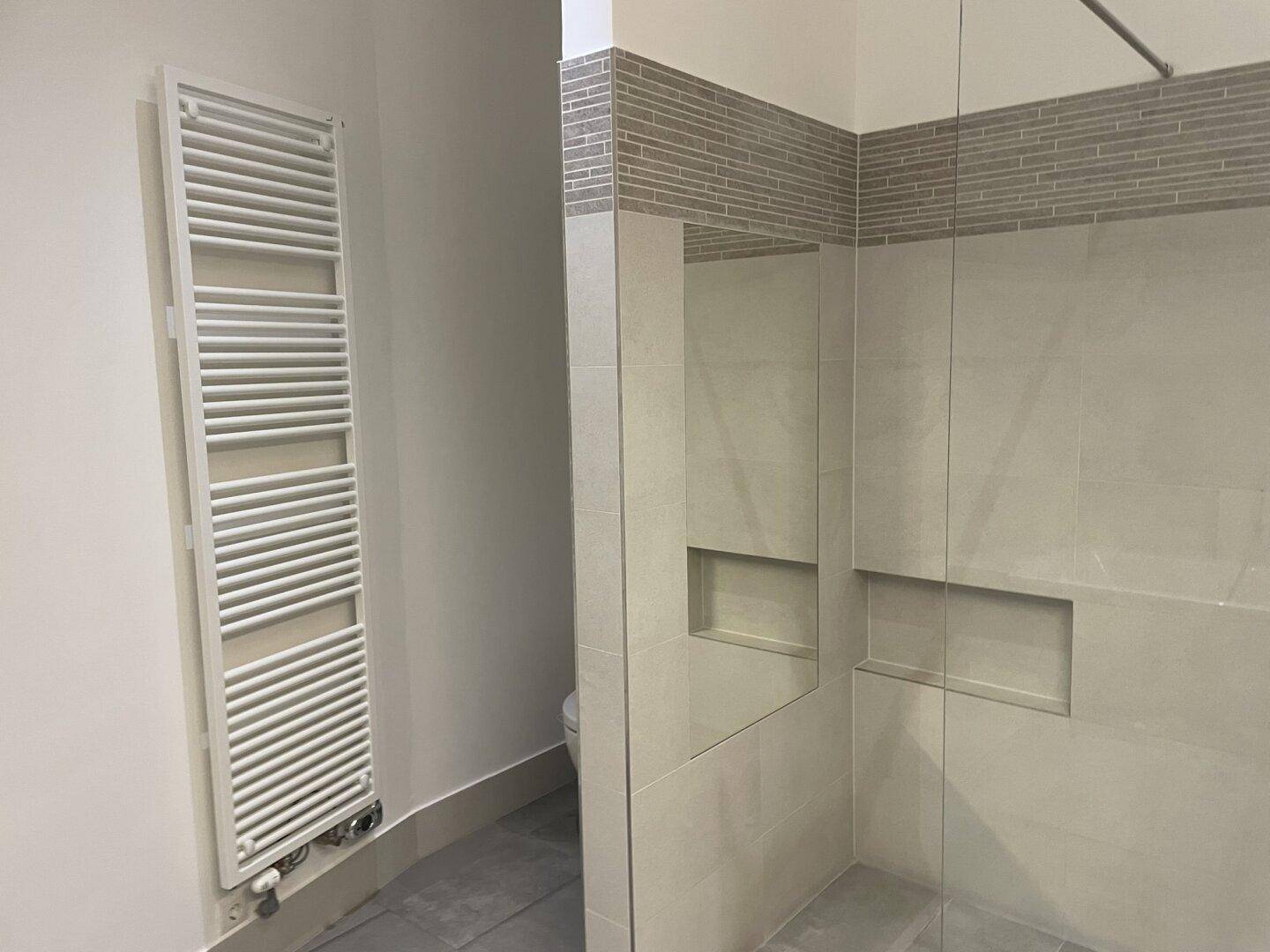 Begehbare Dusche mit Glaswand und praktischem Handtuchheizkörper im Badezimmer.