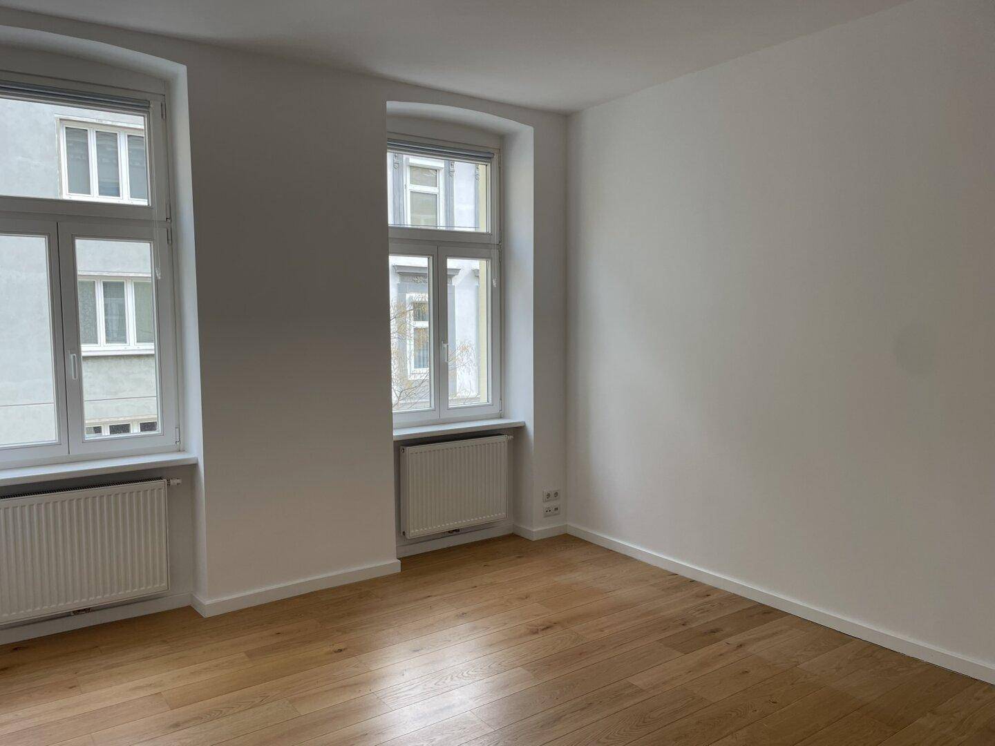 Geräumiges Zimmer mit Parkettboden und viel Tageslicht durch zwei Fenster.