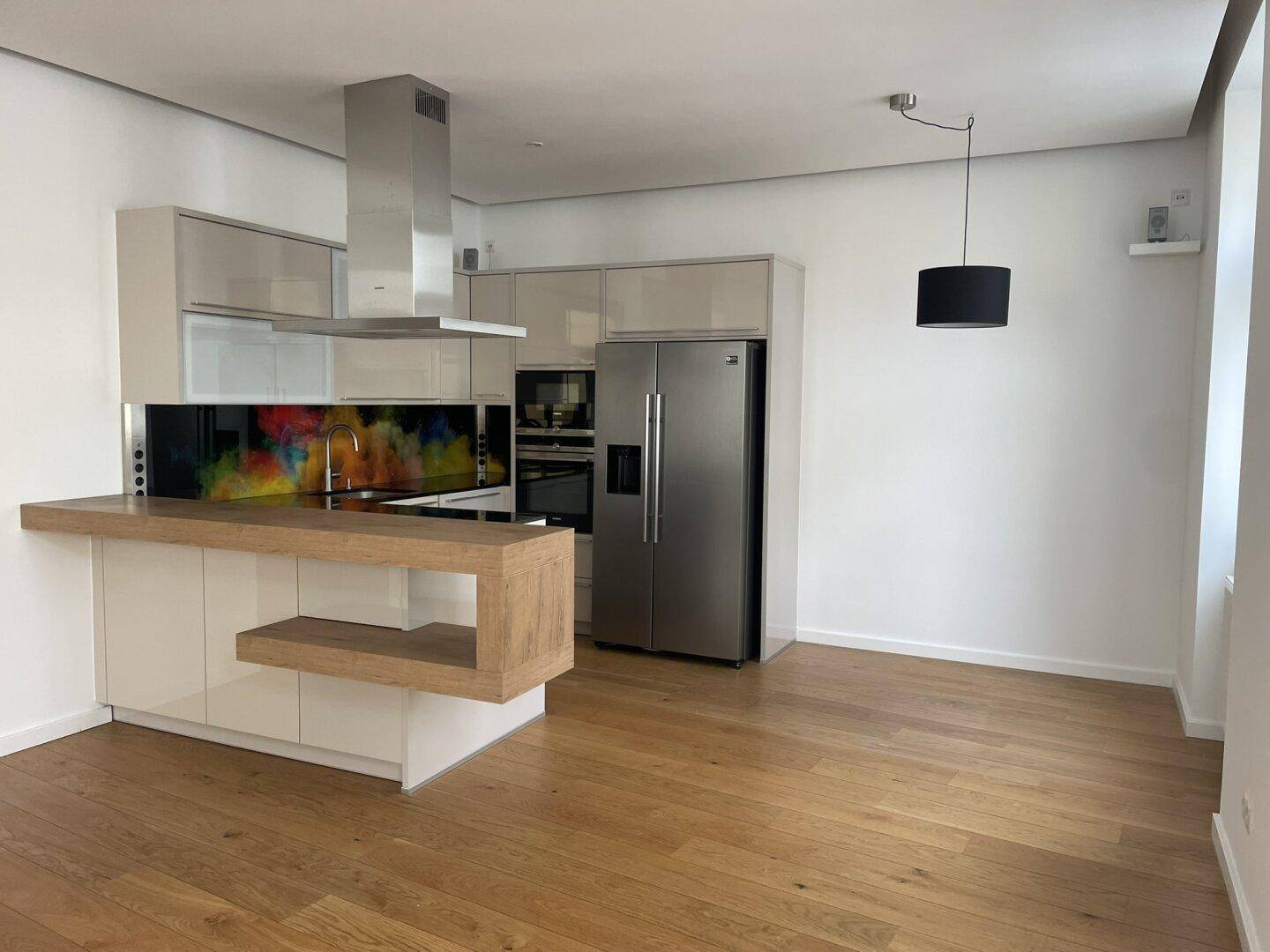 Moderne Einbauküche mit Edelstahlgeräten, Kochinsel und hellem Holzparkettboden.