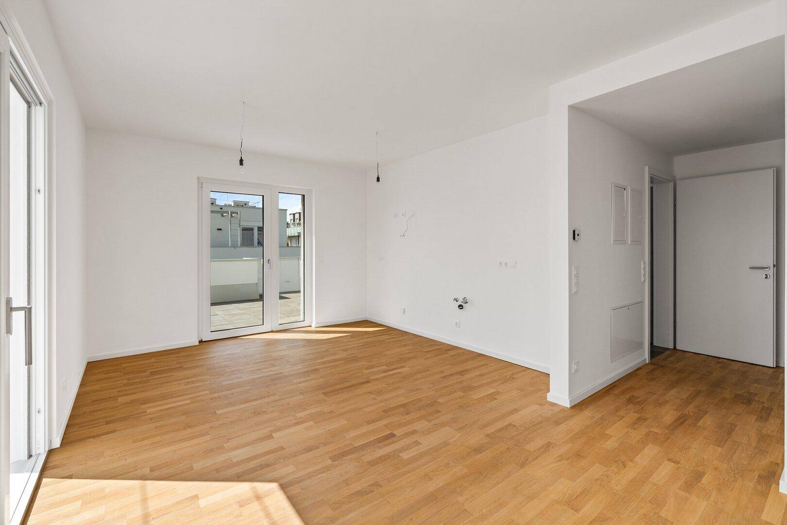 Helles, leeres Wohnzimmer mit Parkettboden und Zugang zu einer großen Terrasse.