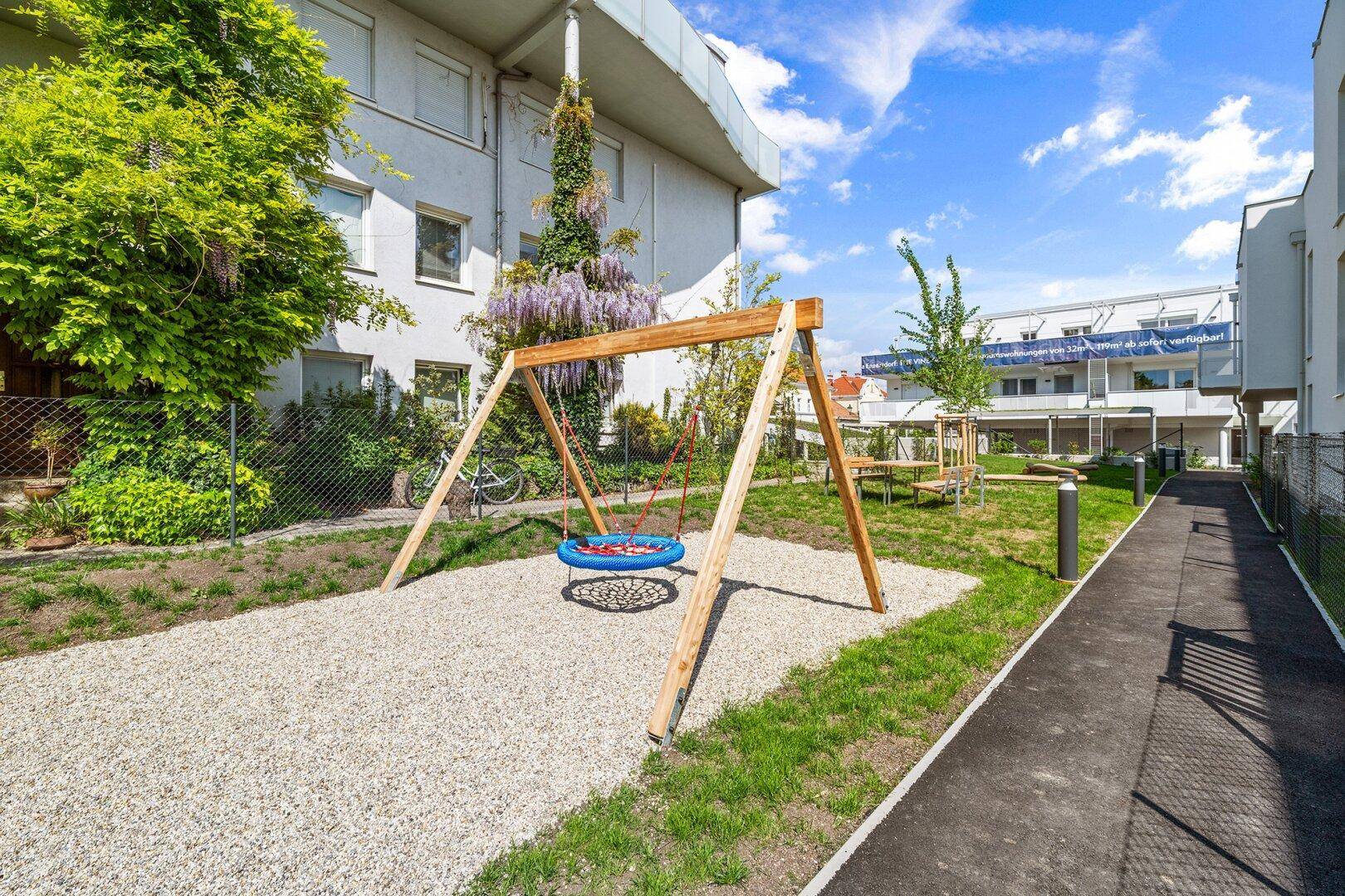 Kinderspielplatz mit Schaukel und Kiesfläche im gemeinschaftlichen Gartenbereich der Wohnanlage.