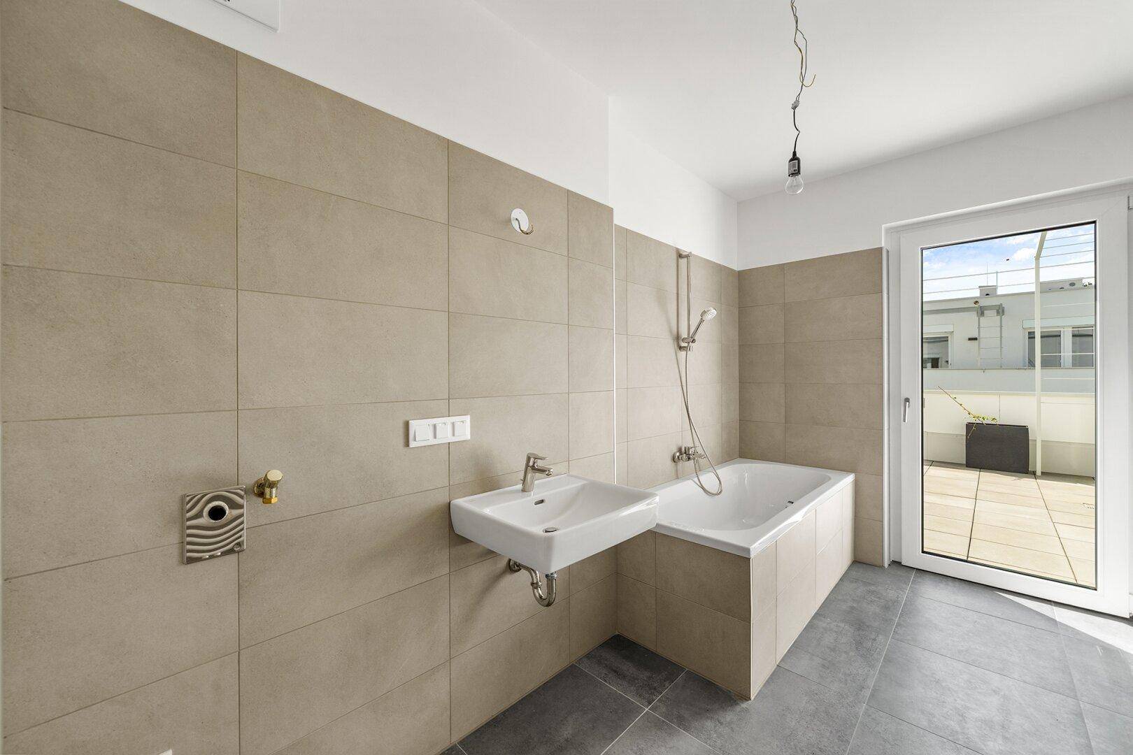 Modernes Badezimmer mit beigefarbenen Fliesen, Badewanne und Zugang zur Terrasse.