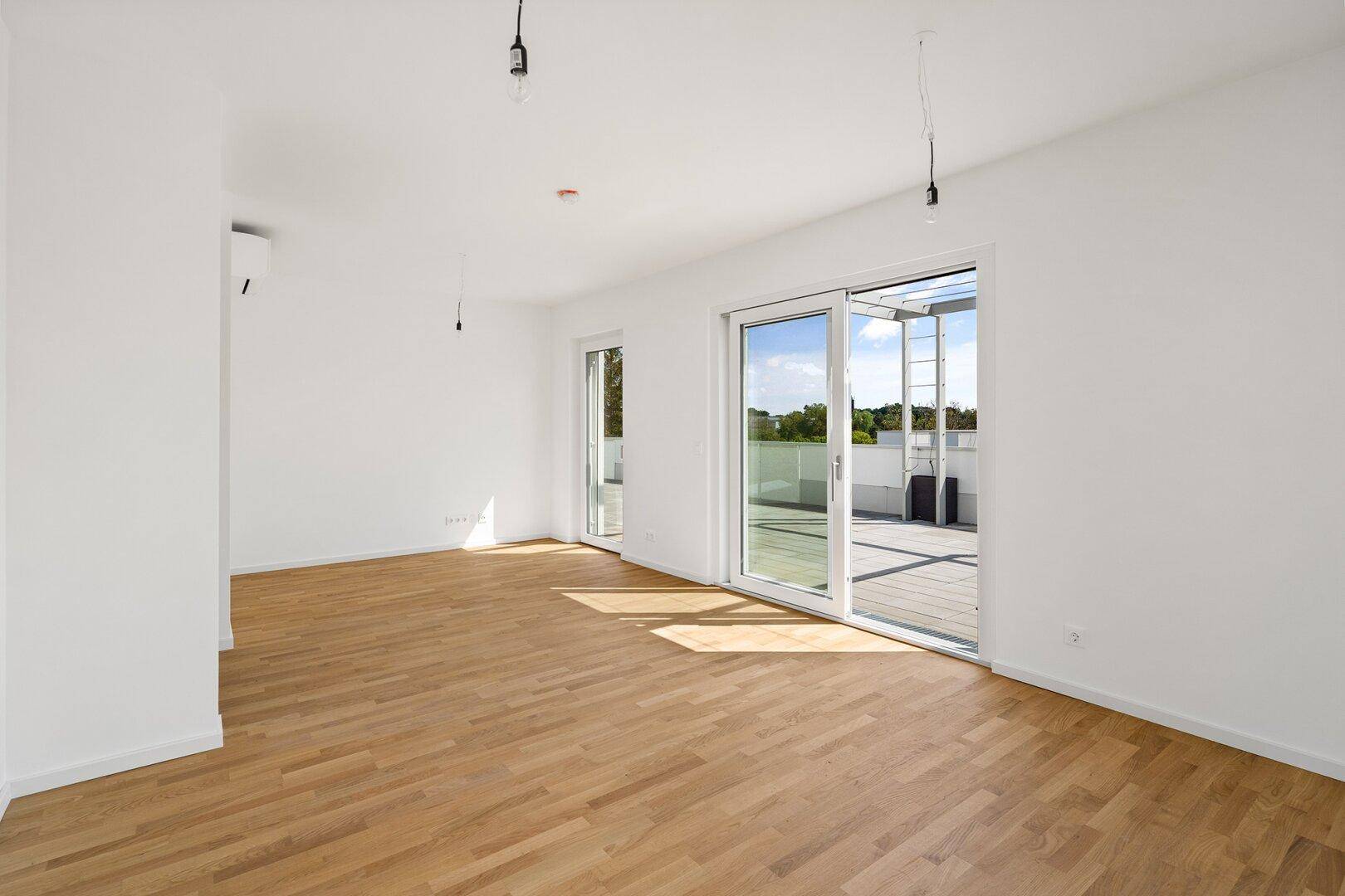 Lichtdurchflutetes Wohnzimmer mit Holzboden und Schiebetür zur Dachterrasse.
