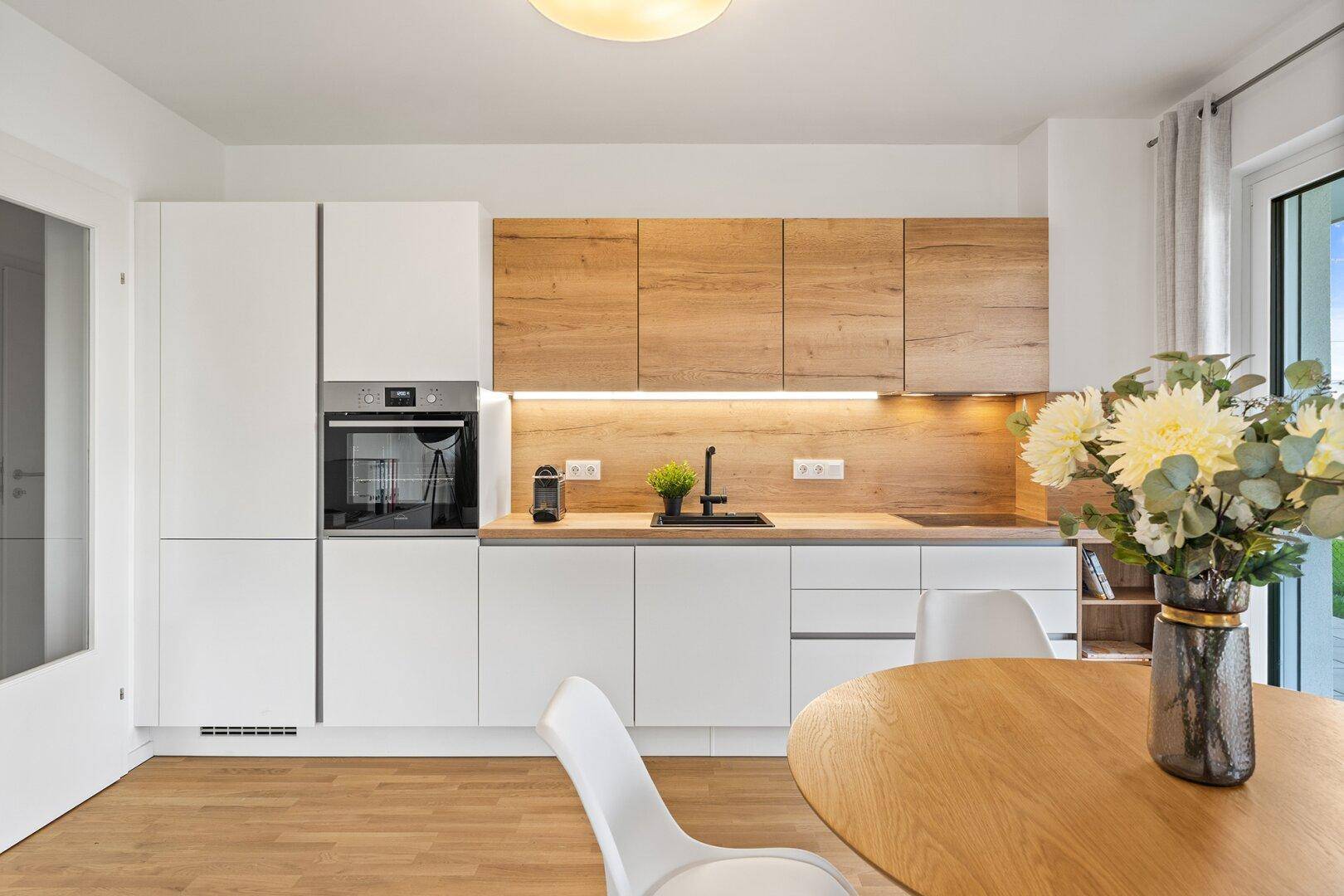 Moderne Einbauküche mit weißen und holzfarbenen Fronten sowie integrierten Geräten.