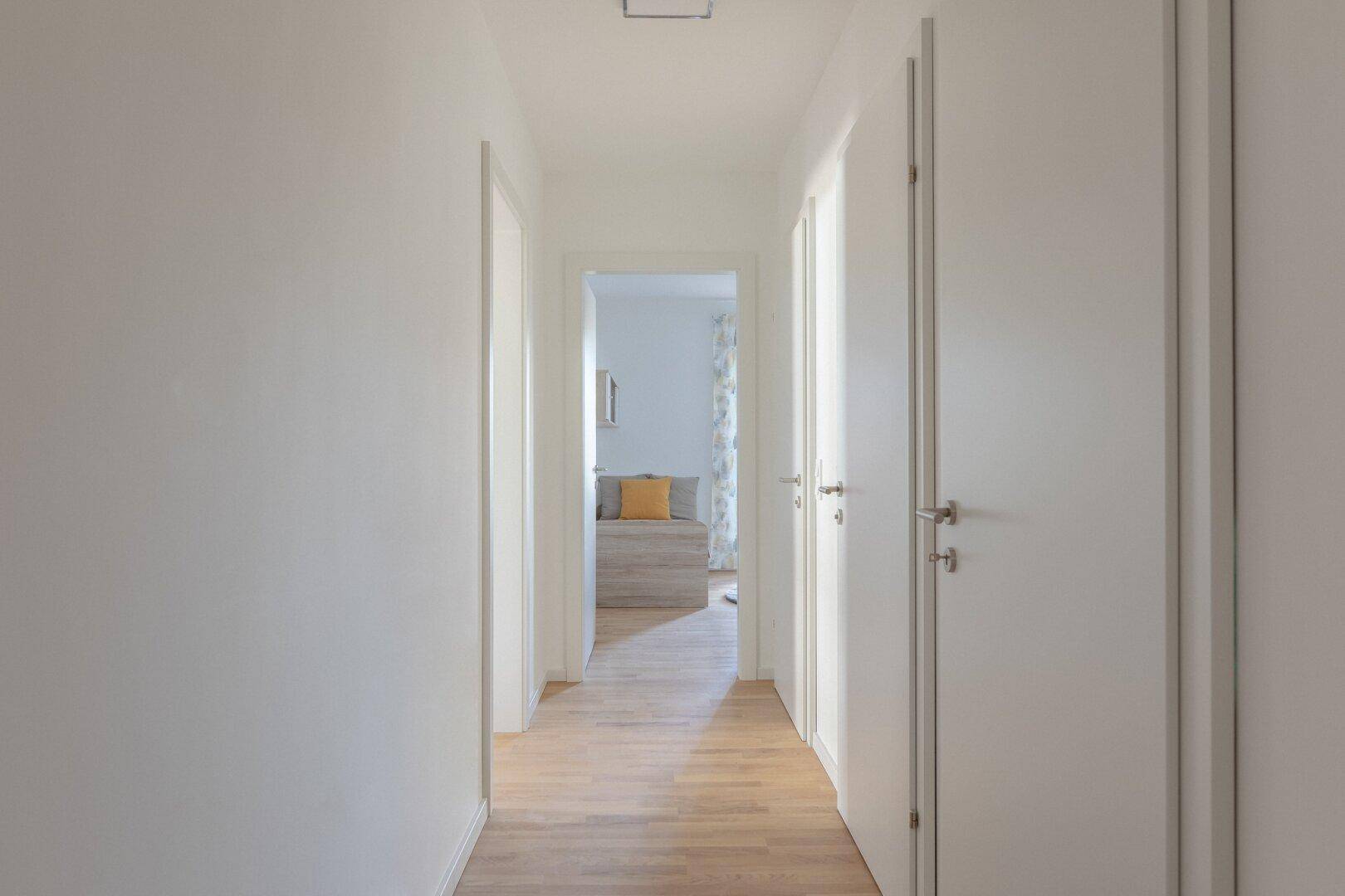 Heller Flur mit Holzboden und weißen Türen, der zu den Zimmern führt.