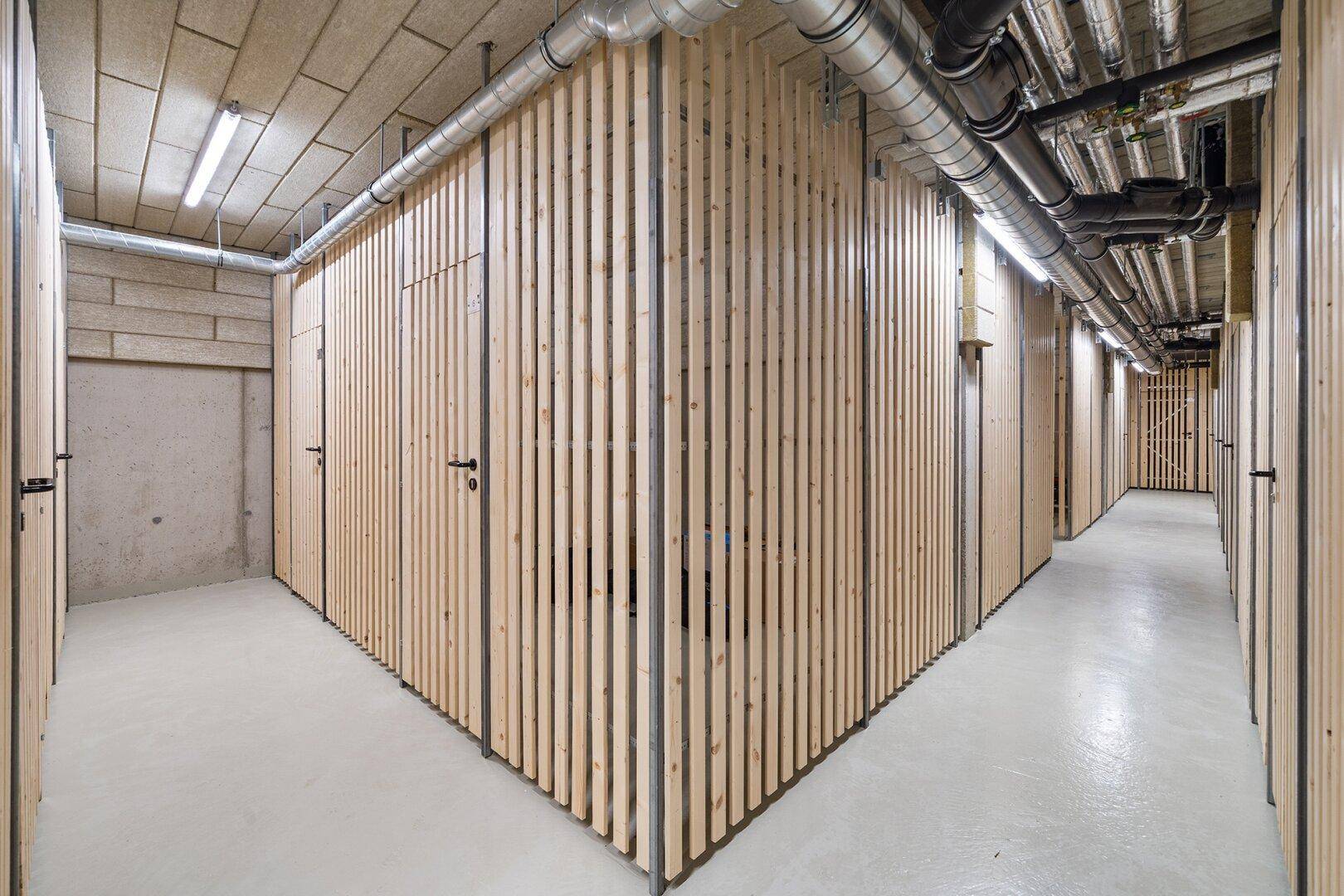 Kellerabteile mit Holzlamellenwänden und sichtbaren Installationen im Untergeschoss.