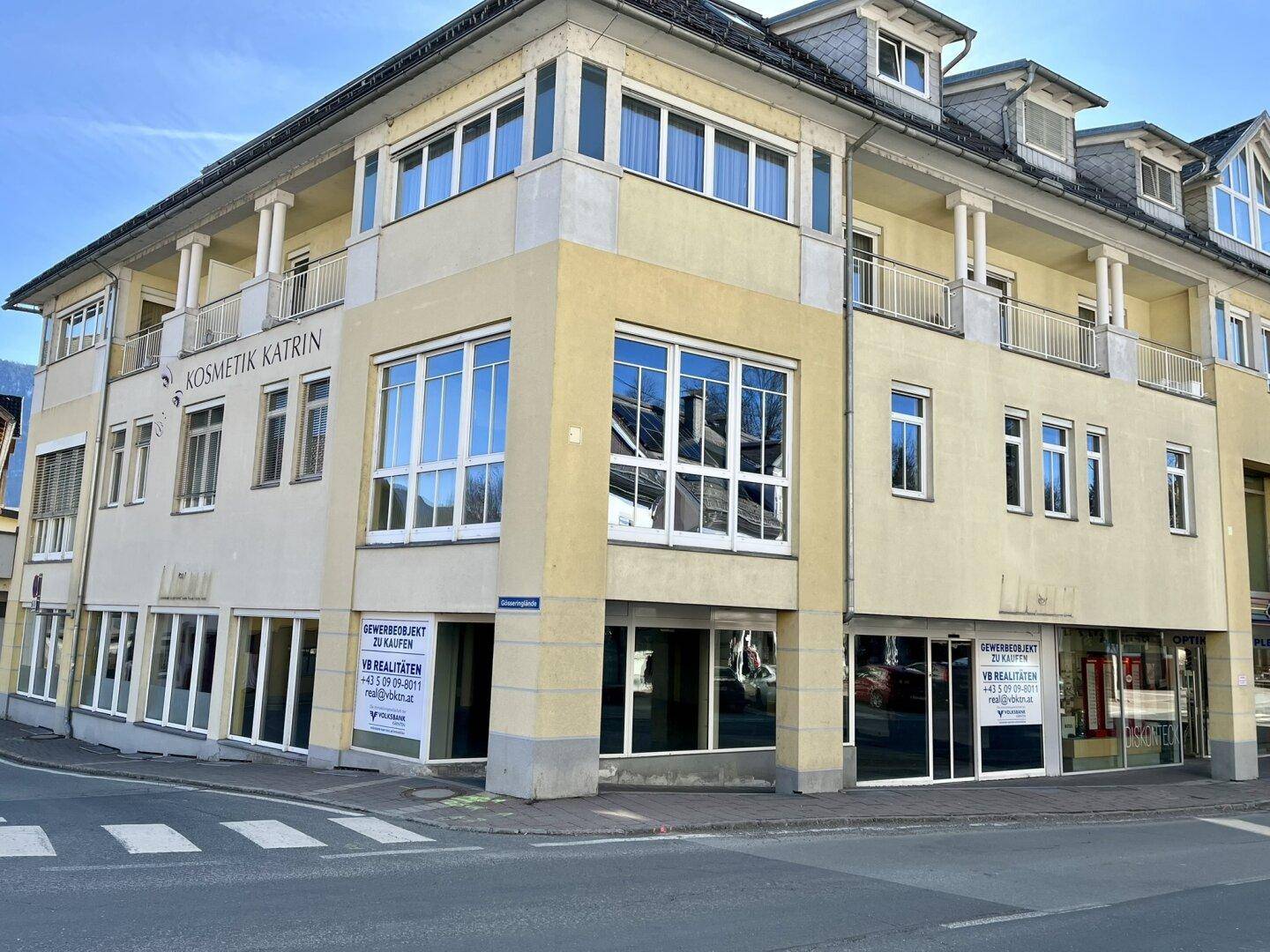 Eckgebäude mit mehreren Etagen, großen Fenstern und Balkonen an einer städtischen Kreuzung.