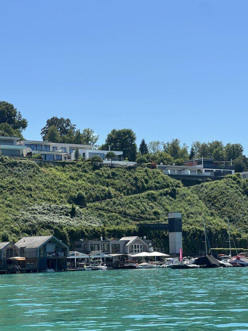 Moderne Villen auf einem grünen Hügel mit Blick auf den See und private Bootshäuser.