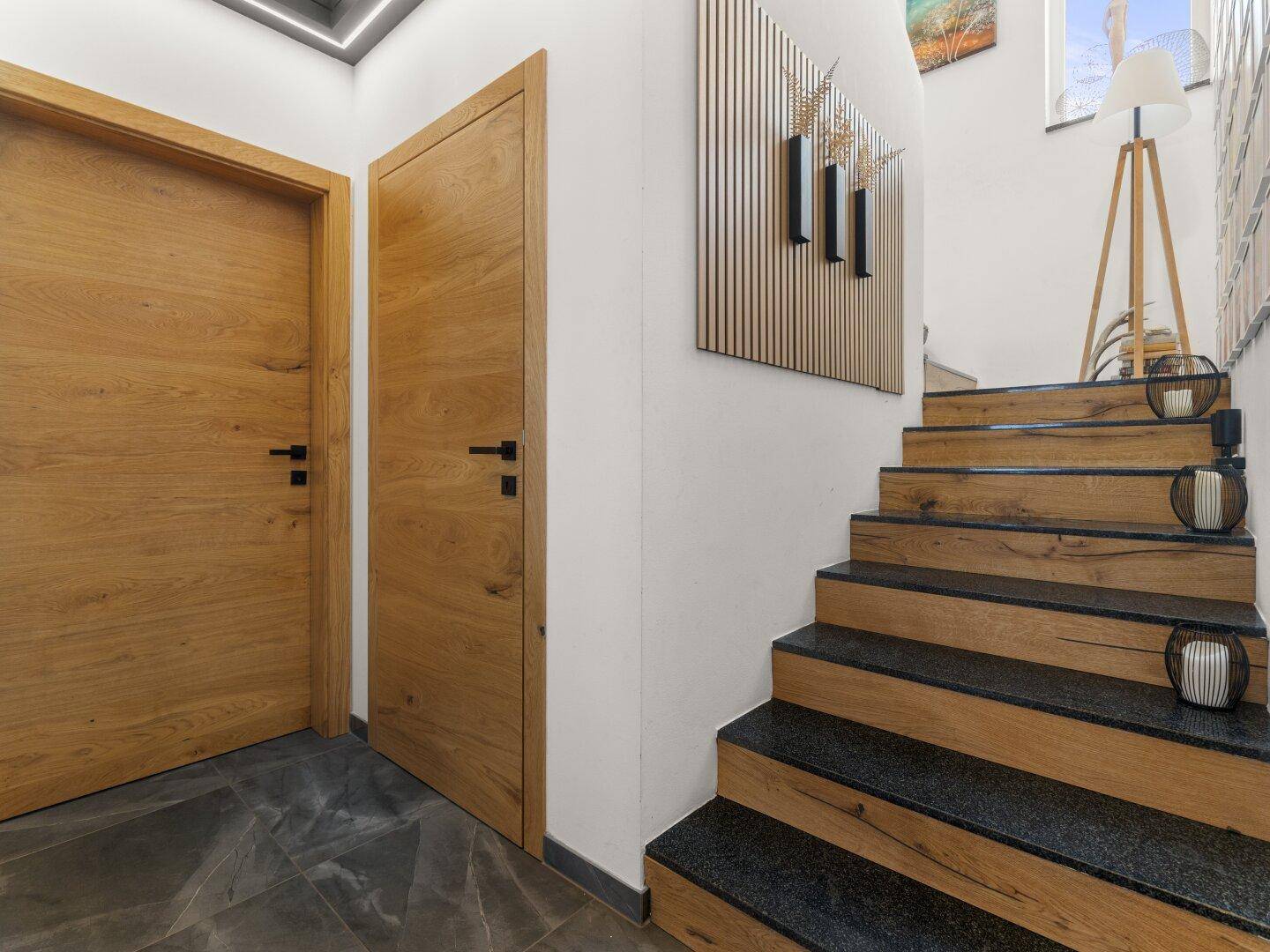 Moderner Treppenaufgang mit Holzstufen und dunklem Granit, daneben Holztüren.
