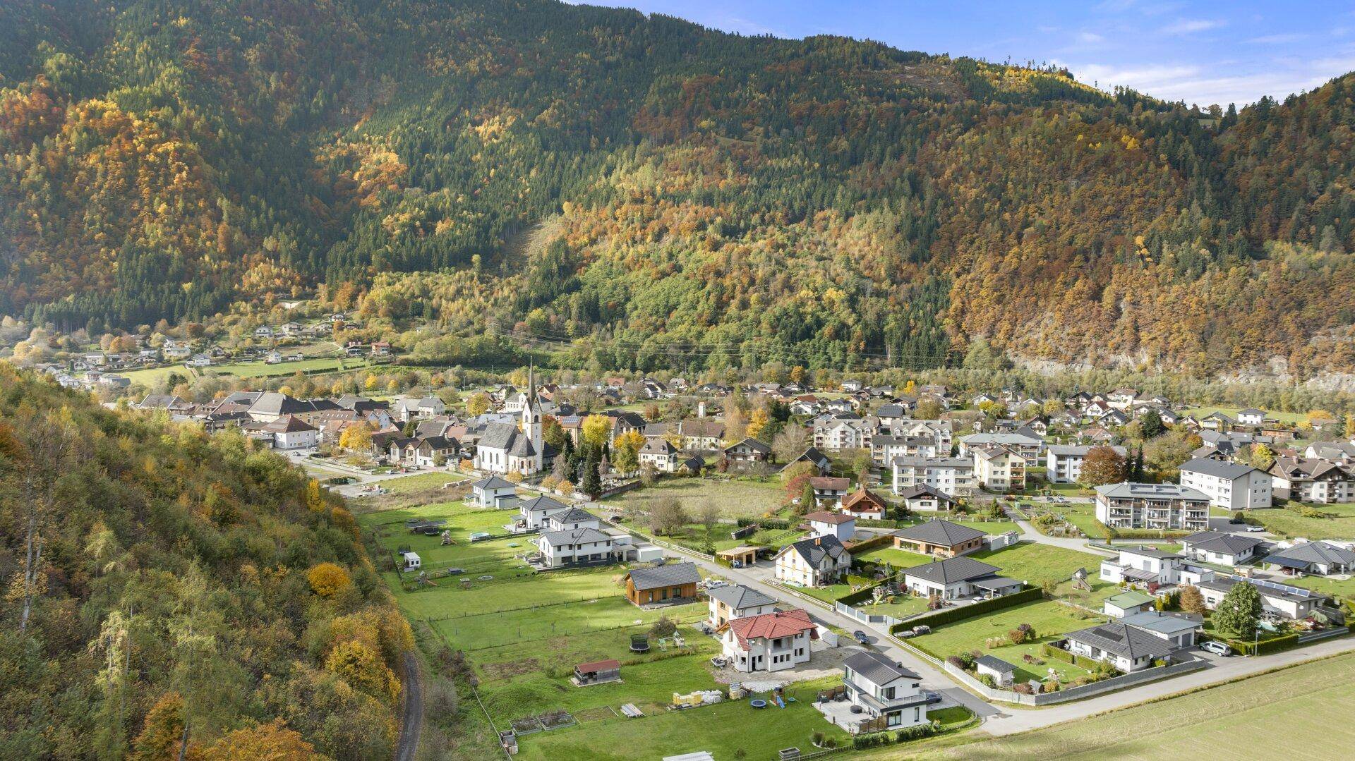 Malerische Luftaufnahme einer Siedlung umgeben von bewaldeten Bergen im Herbst.