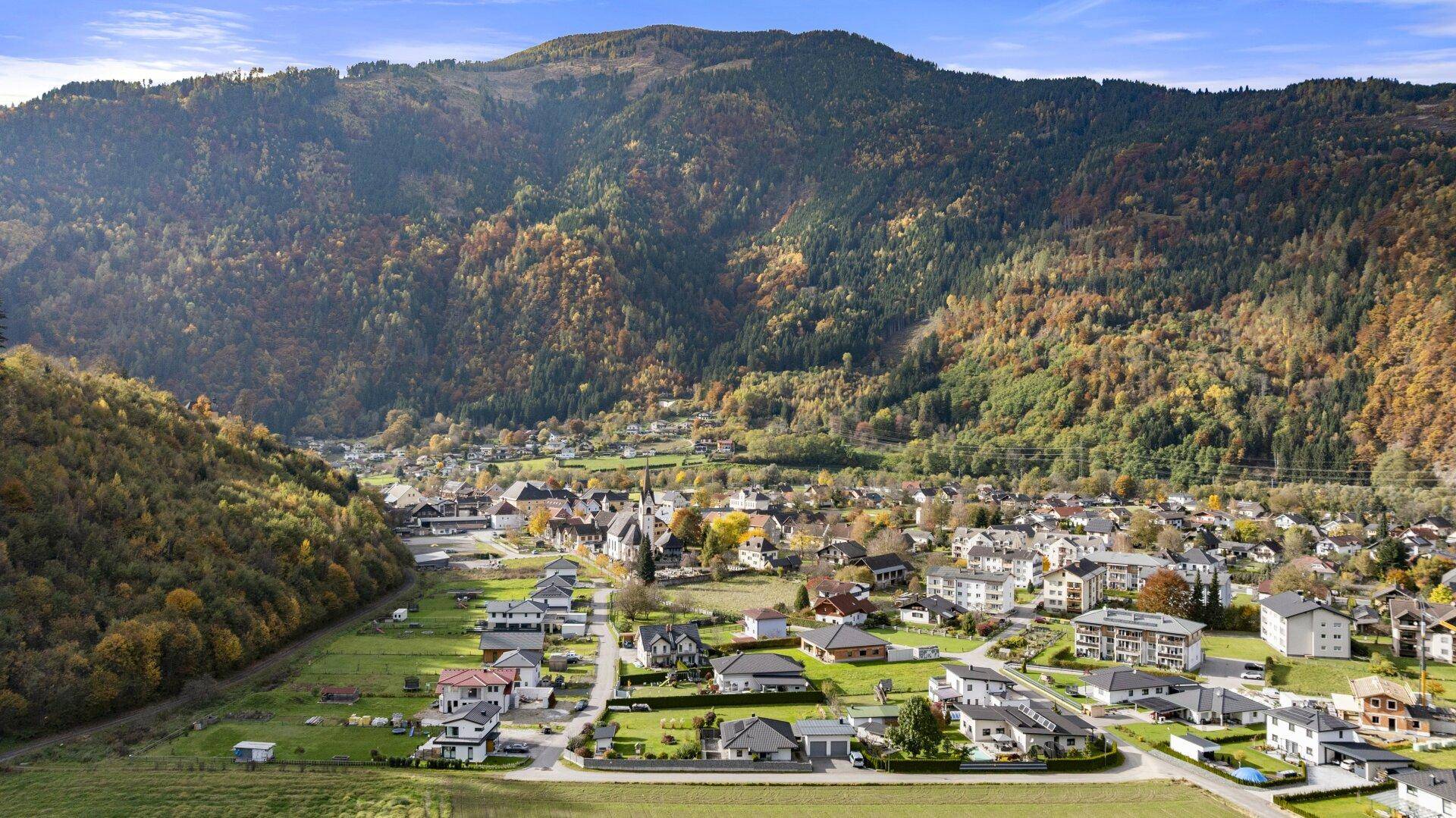 Weitläufige Luftaufnahme einer Wohnsiedlung eingebettet in eine herbstliche Berglandschaft.
