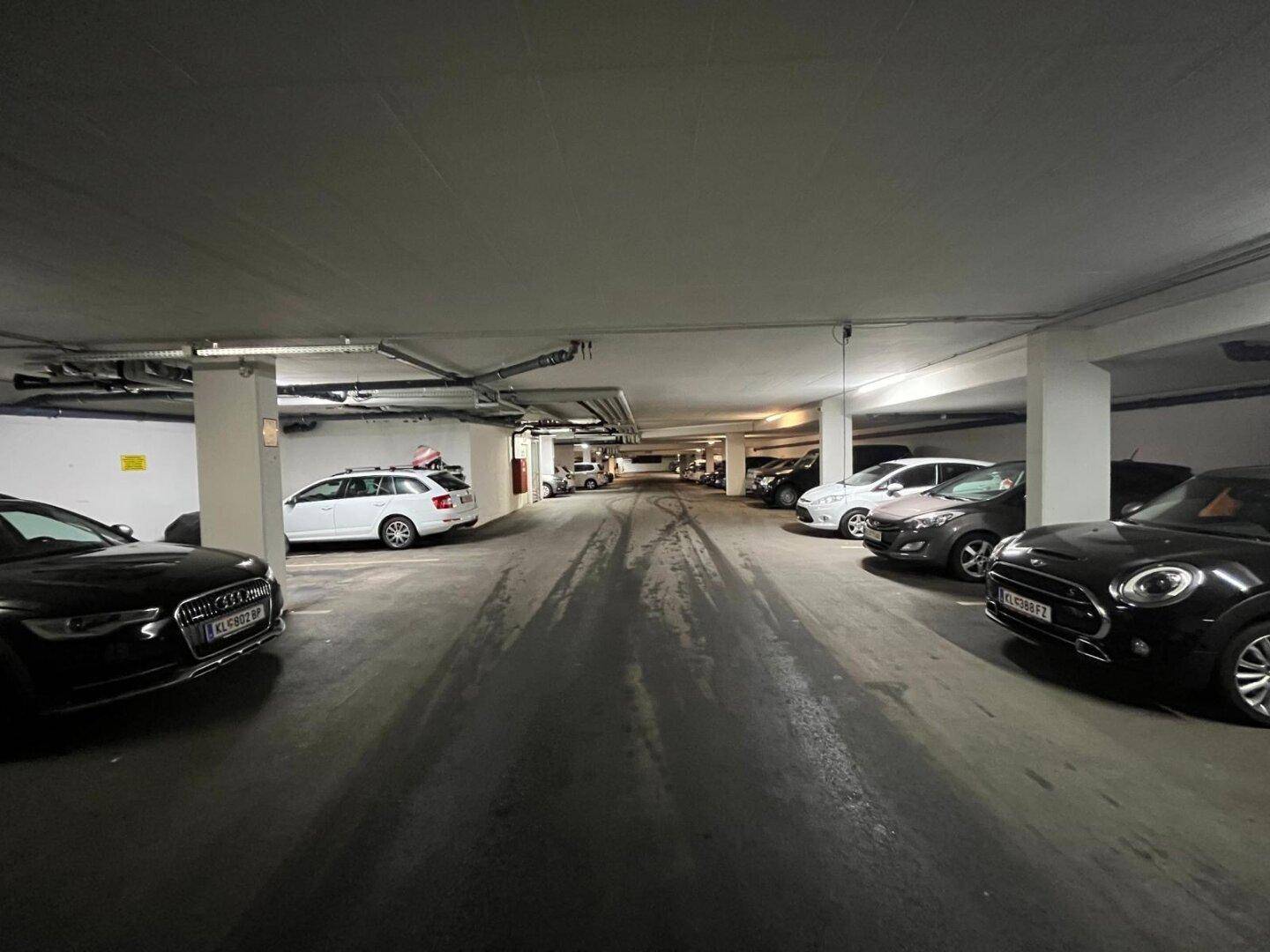 Breite Tiefgarage mit vielen geparkten Autos und sauberem Betonboden unter künstlicher Beleuchtung.