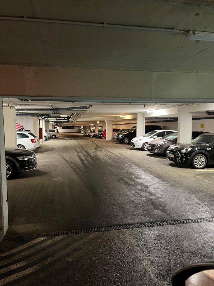 Übersichtliche Tiefgarage mit markierten Stellplätzen und Entwässerungsrinnen im Bodenbereich.