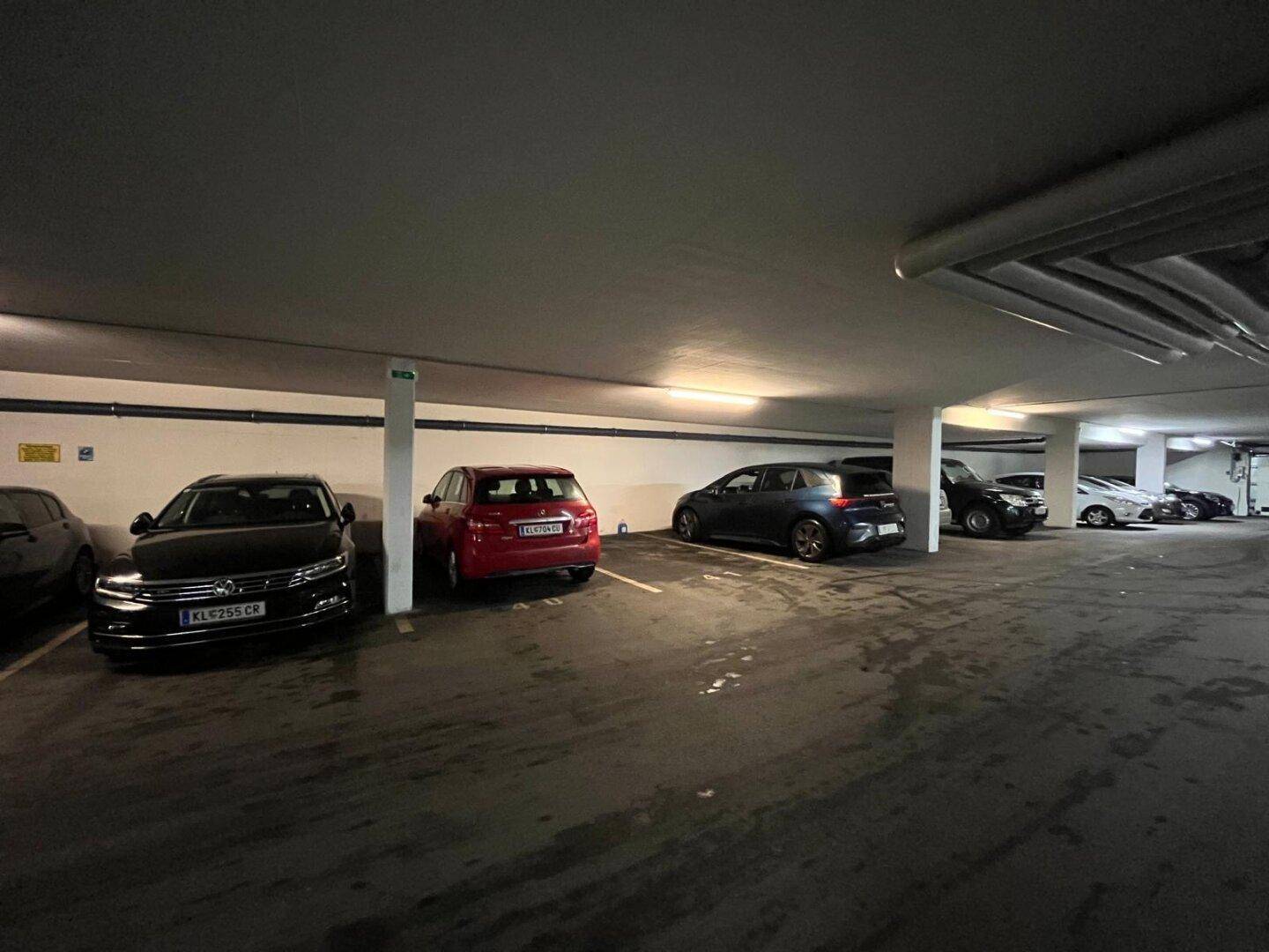 Heller Bereich der Tiefgarage mit mehreren geparkten Fahrzeugen und klaren Markierungen auf dem Boden.