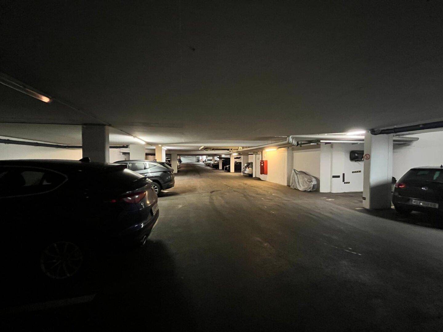 Langer Gang in der Tiefgarage mit Reihen von geparkten Autos und Deckenbeleuchtung.