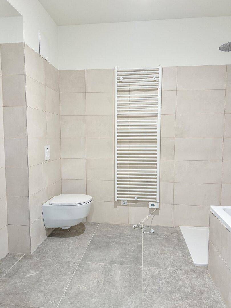 Helles Badezimmer mit modernen Fliesen, wandhängendem WC und beheiztem Handtuchhalter.