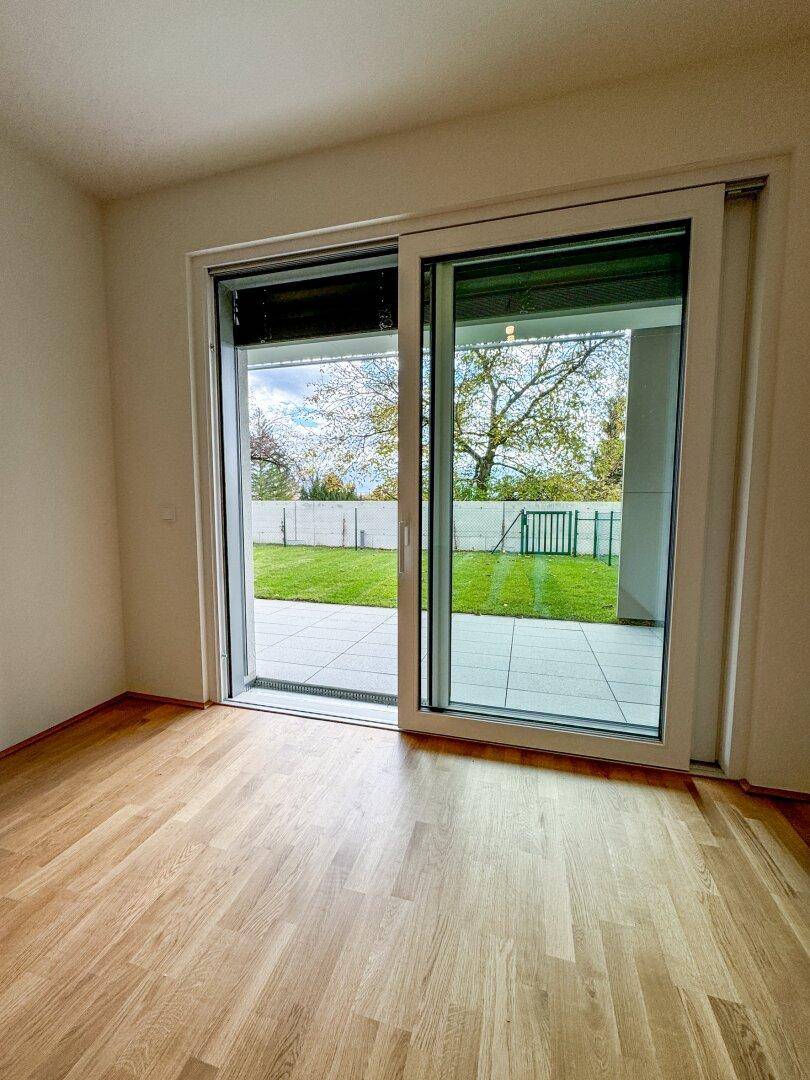 Lichtdurchfluteter Raum mit Holzboden und großem Schiebefenster zum Garten und zur Terrasse.