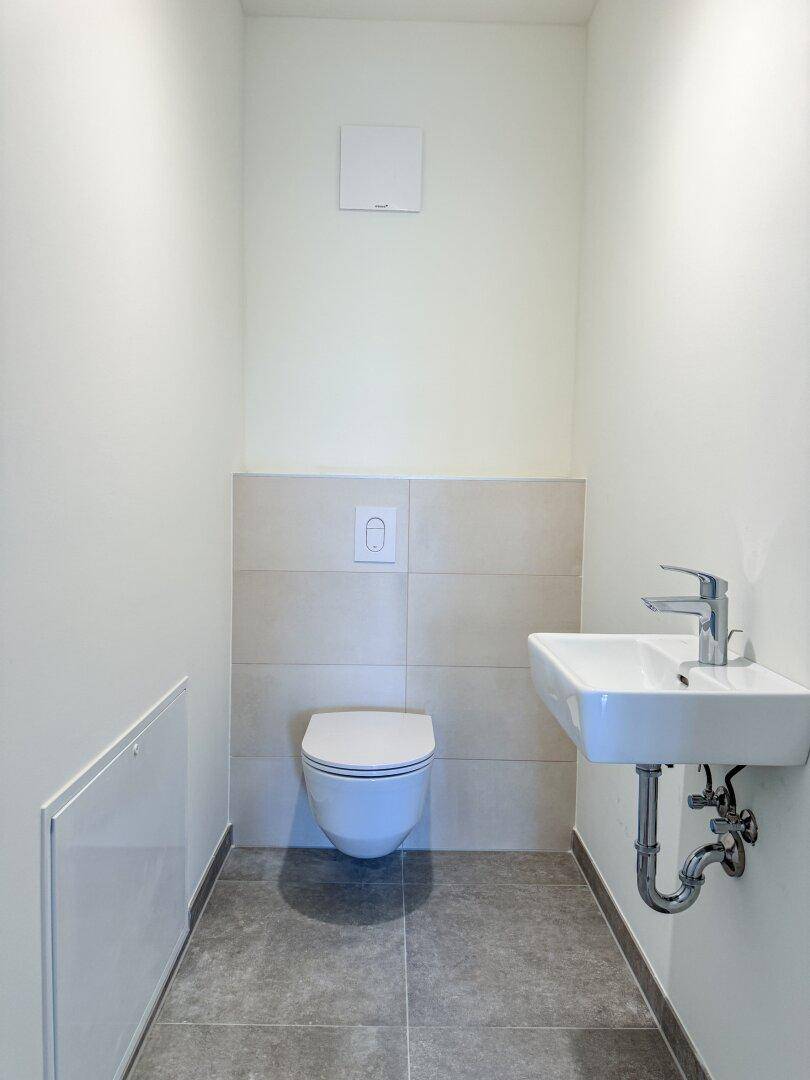 Kompaktes Gäste-WC mit wandhängendem WC, kleinem Waschbecken und modernen Fliesen.