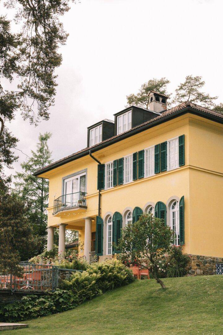 Klassische Villa mit gelber Fassade, grünen Fensterläden und gepflegtem Vorgartenbereich.