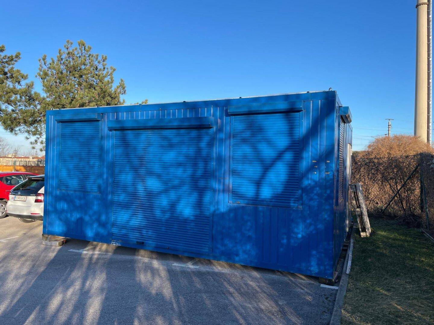 Seitenansicht des blauen Containergebäudes mit drei Fenstern, die alle mit Rollläden versehen sind.