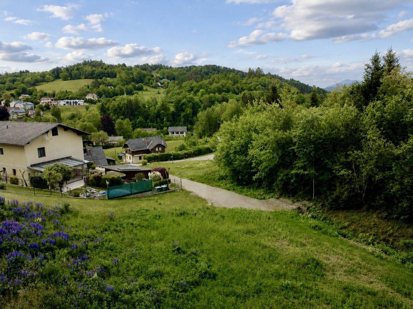 Panoramablick auf eine ländliche Siedlung in einem grünen Tal mit bewaldeten Hügeln.