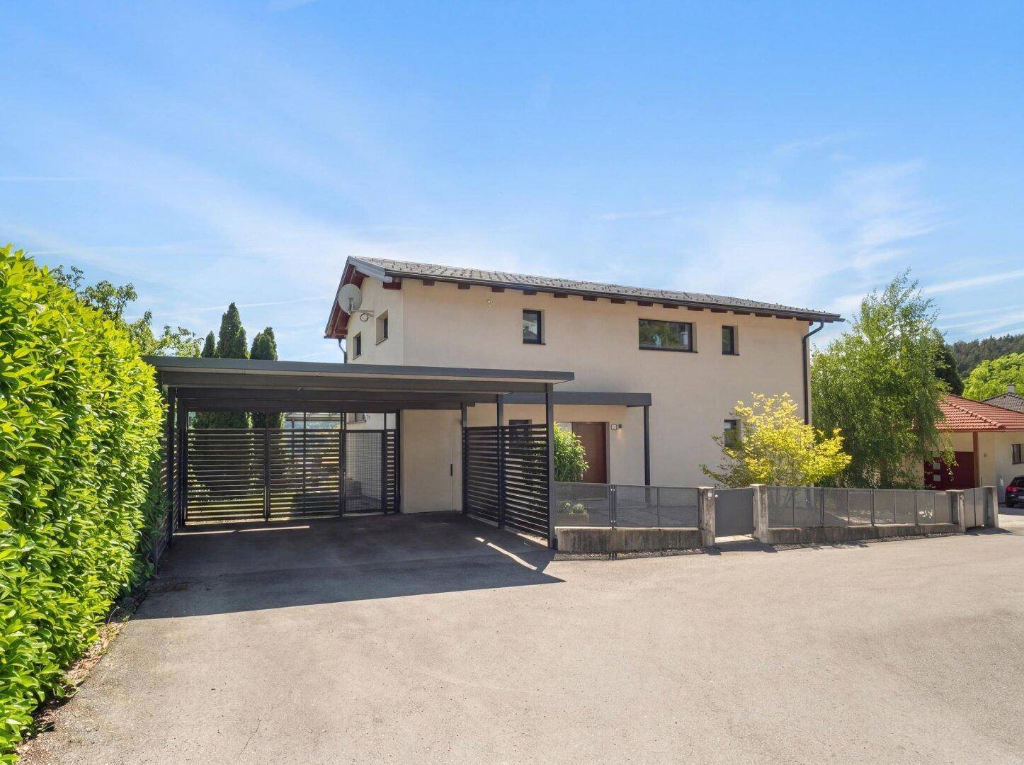 Vorderansicht des Hauses mit modernem Carport und gepflegter Hecke unter blauem Himmel.