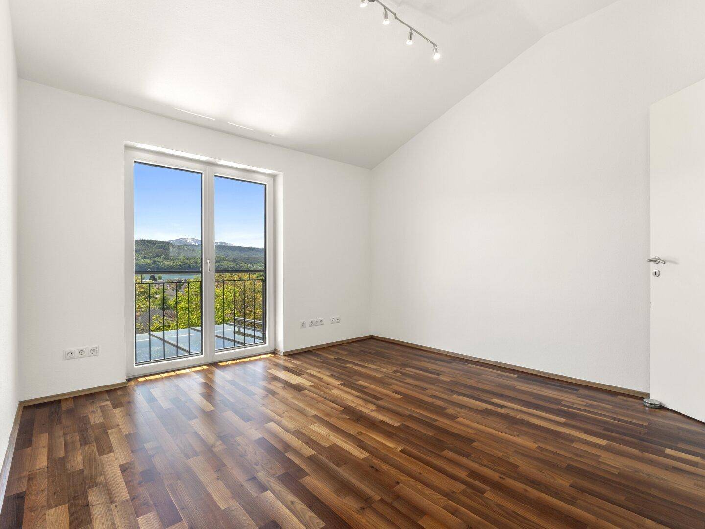 Helles Schlafzimmer mit Holzboden und Balkonzugang mit Bergblick.