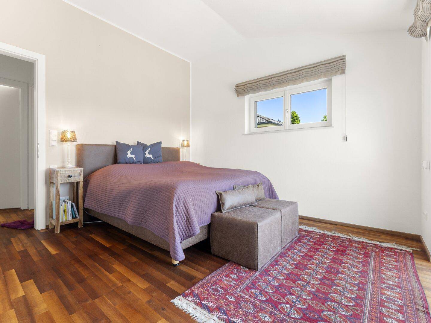 Schlafzimmer mit Holzboden, Doppelbett und einem Fenster mit Blick nach draußen.