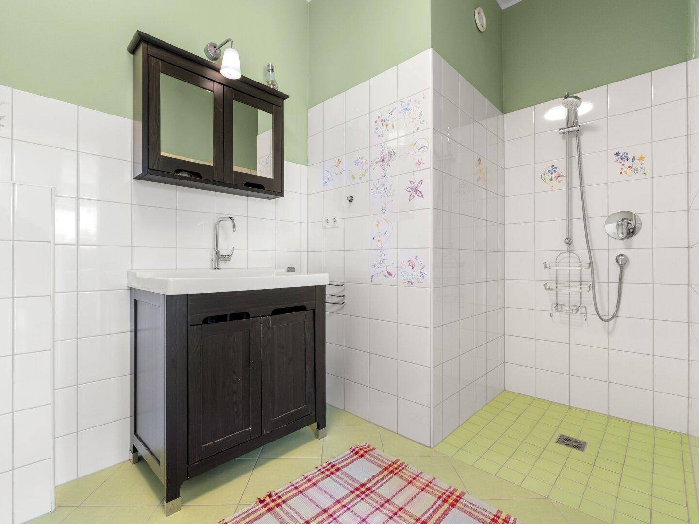 Badezimmer mit Dusche, Waschbecken und farbigen Fliesen an den Wänden.