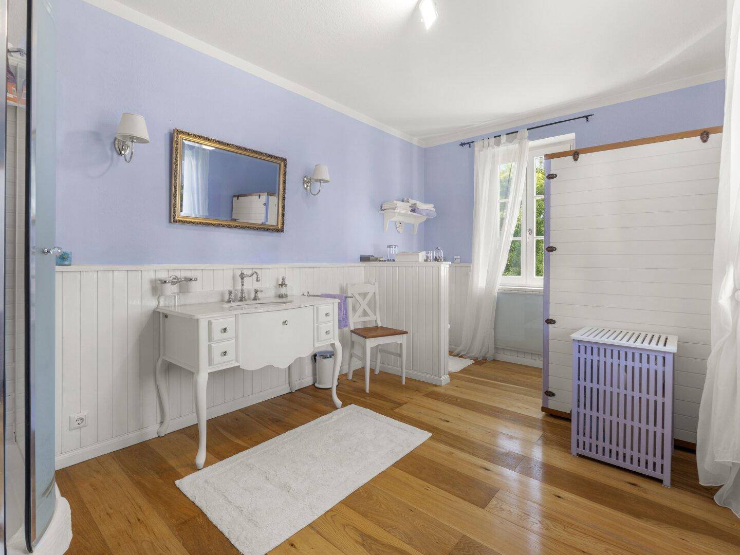 Geräumiges Badezimmer mit hellblauen Wänden, Holzvertäfelung und freistehendem Waschtisch.