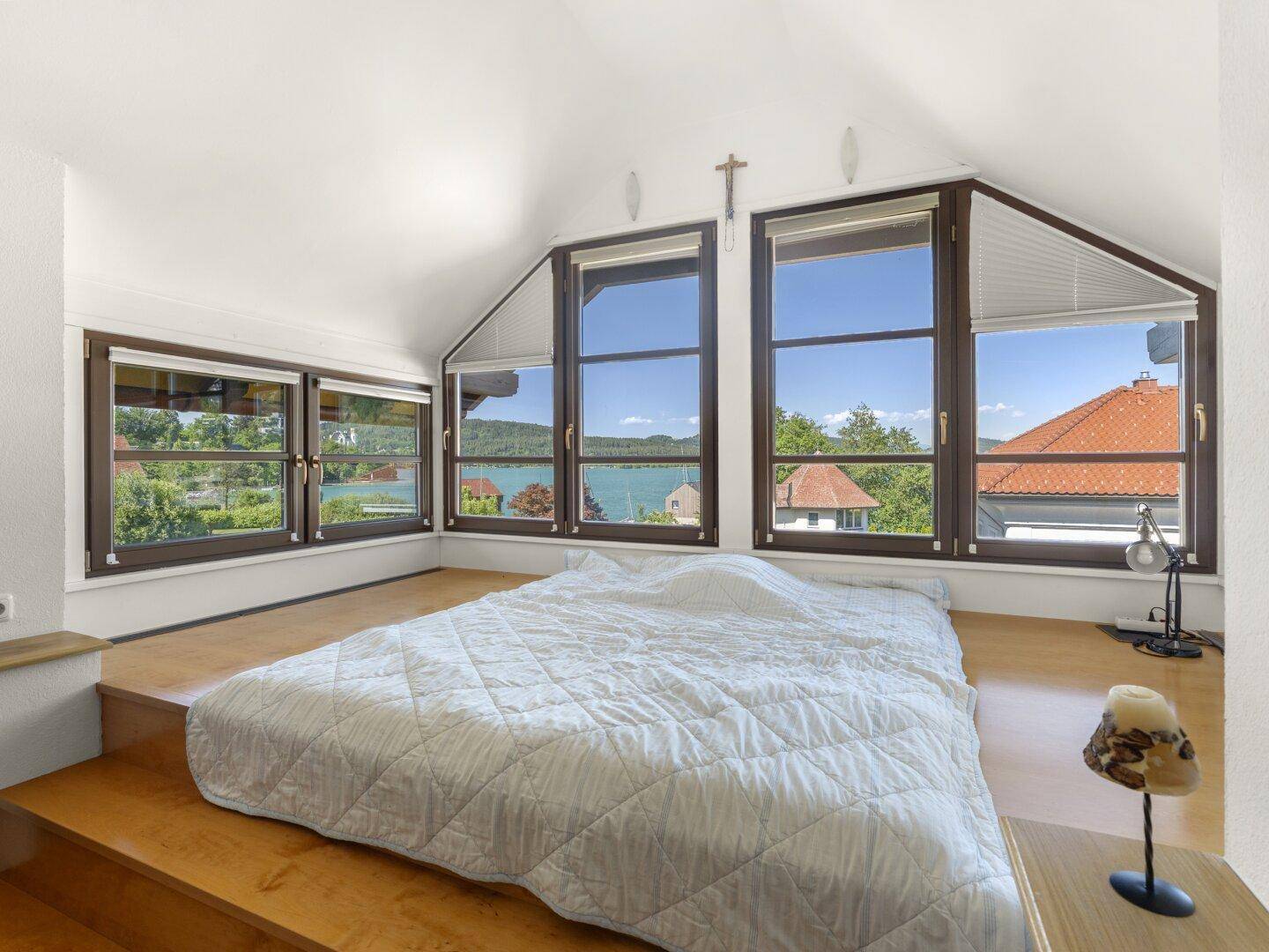 Schlafzimmer mit Panoramablick auf den See, erhöhtem Bett und viel Tageslicht.