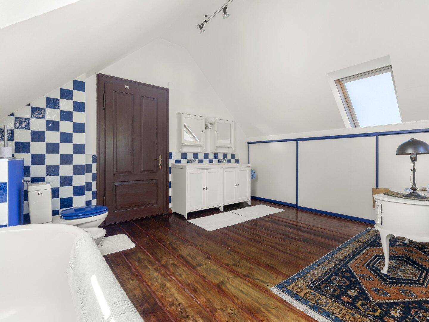Badezimmer im Dachgeschoss mit freistehender Badewanne, blauen Fliesen und Holzboden.