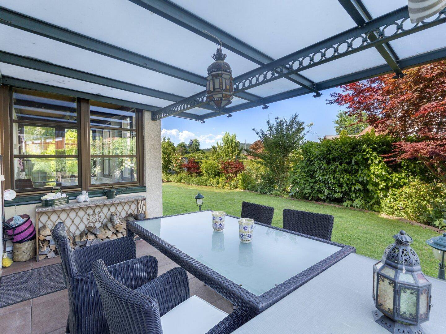 Überdachte Terrasse mit Esstisch und Stühlen, umgeben von einem gepflegten Garten.