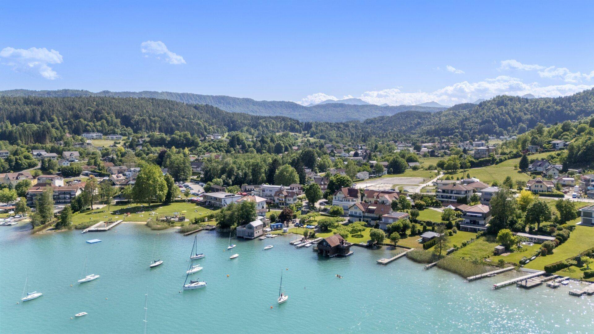 Malerische Luftaufnahme der Seenlandschaft mit umliegenden Häusern und grünen Bergen.